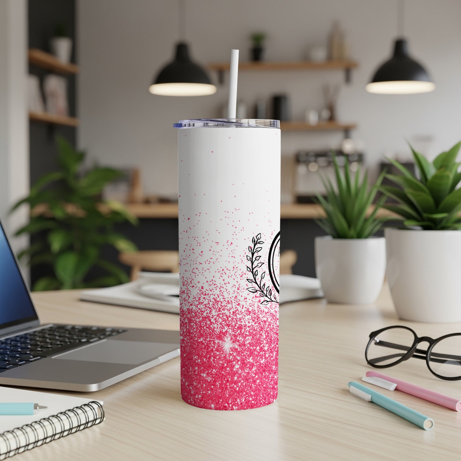 White tumbler with pink glitter and black floral design on desk.