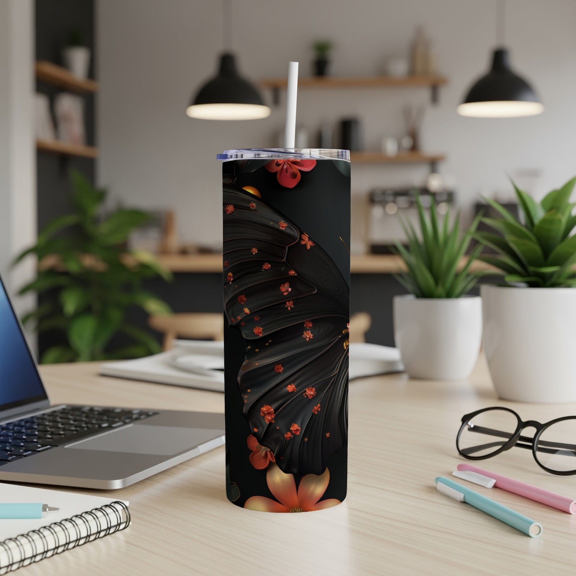 Black tumbler with butterfly wings and floral accents, on a desk.