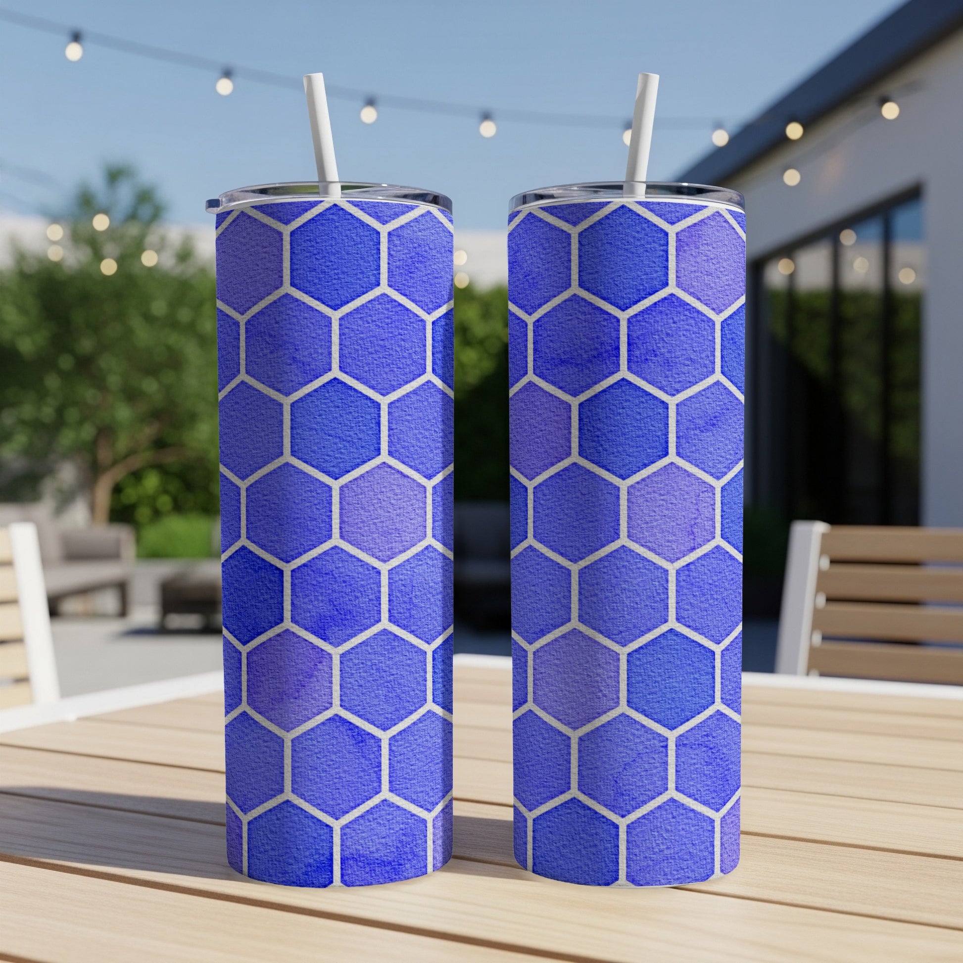 Two blue hexagonal pattern tumblers with white straws on a wooden table outdoors.
