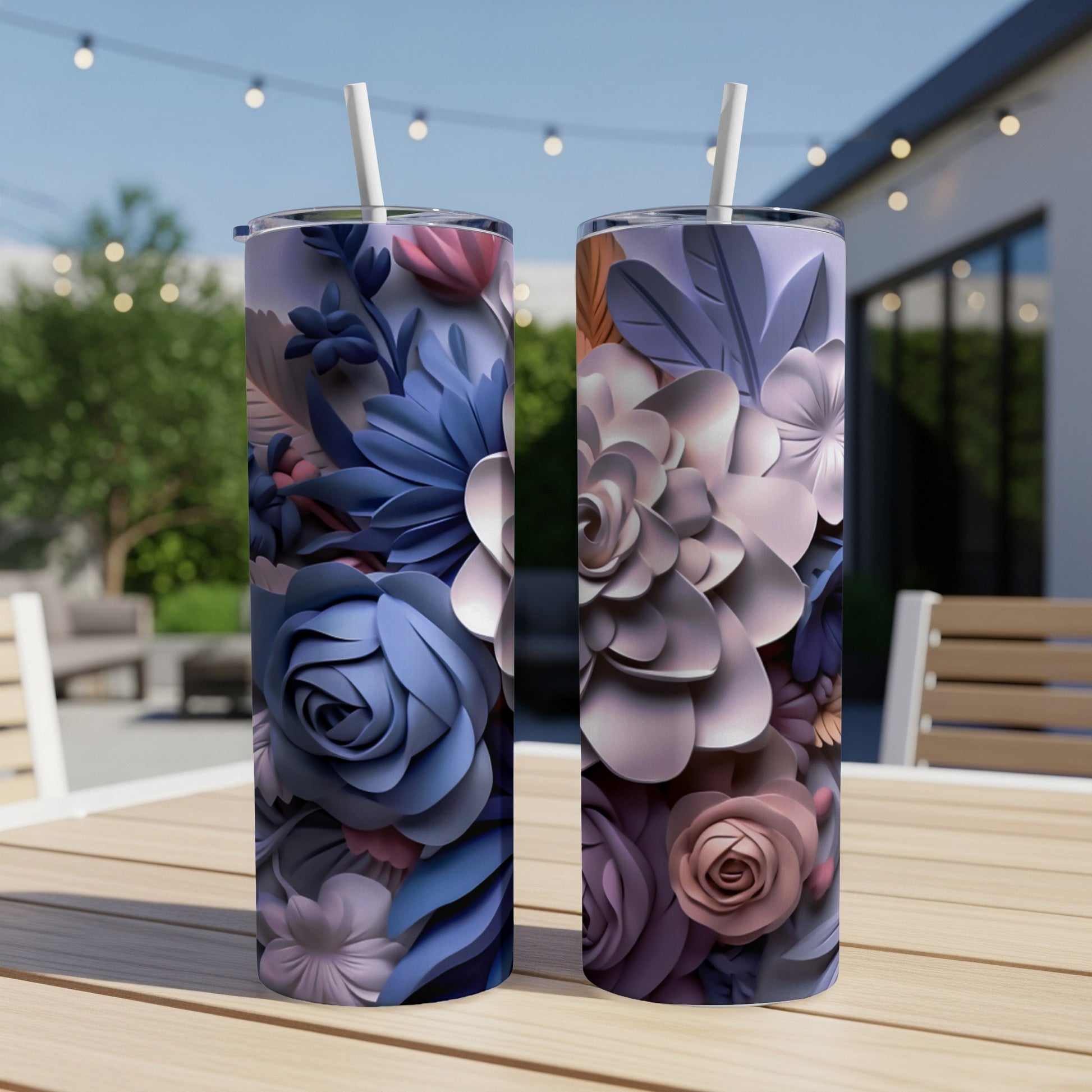 Two tumblers with floral designs sit on a wooden table outdoors.