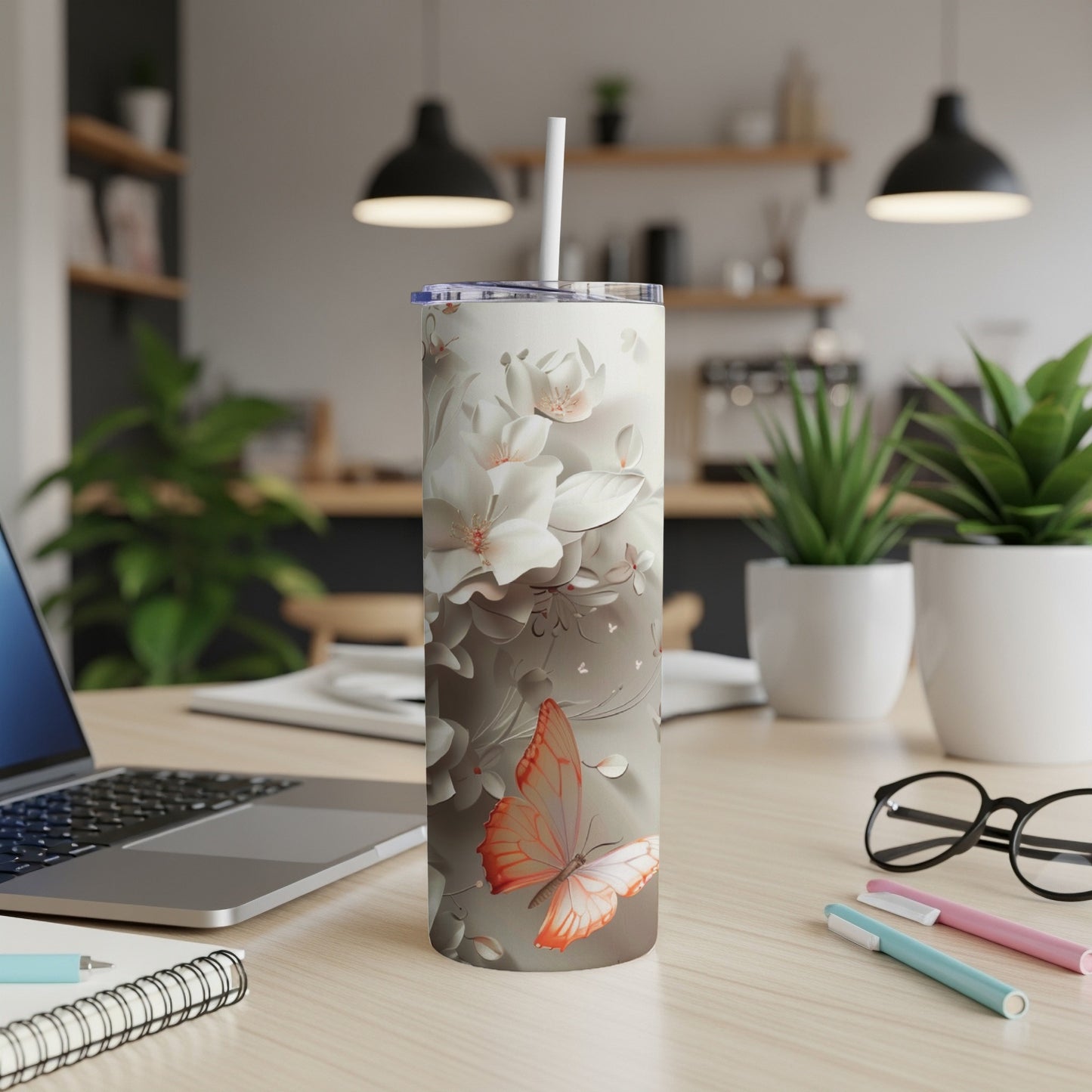 White and orange floral butterfly print tumbler with straw on desk.