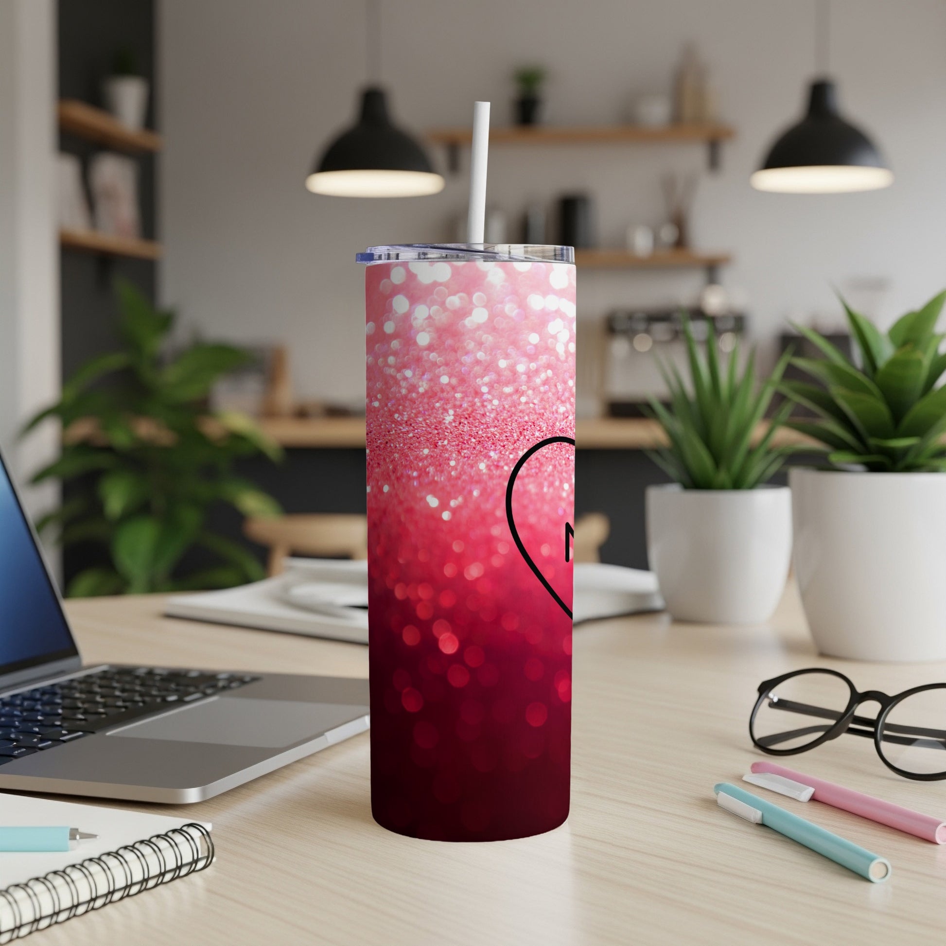 Pink ombre glitter tumbler with black heart and straw on desk.