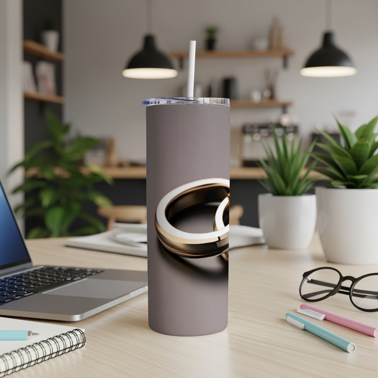 Gray tumbler with gold rings design and straw on a desk.