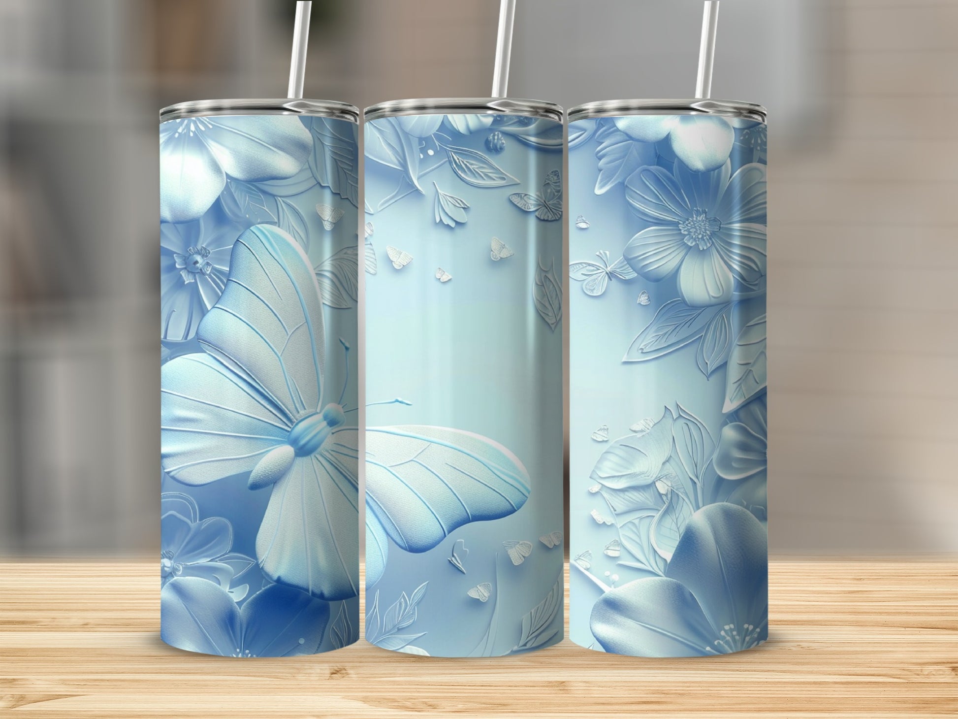 Three pastel blue tumblers with embossed butterflies and flowers on a wooden surface.