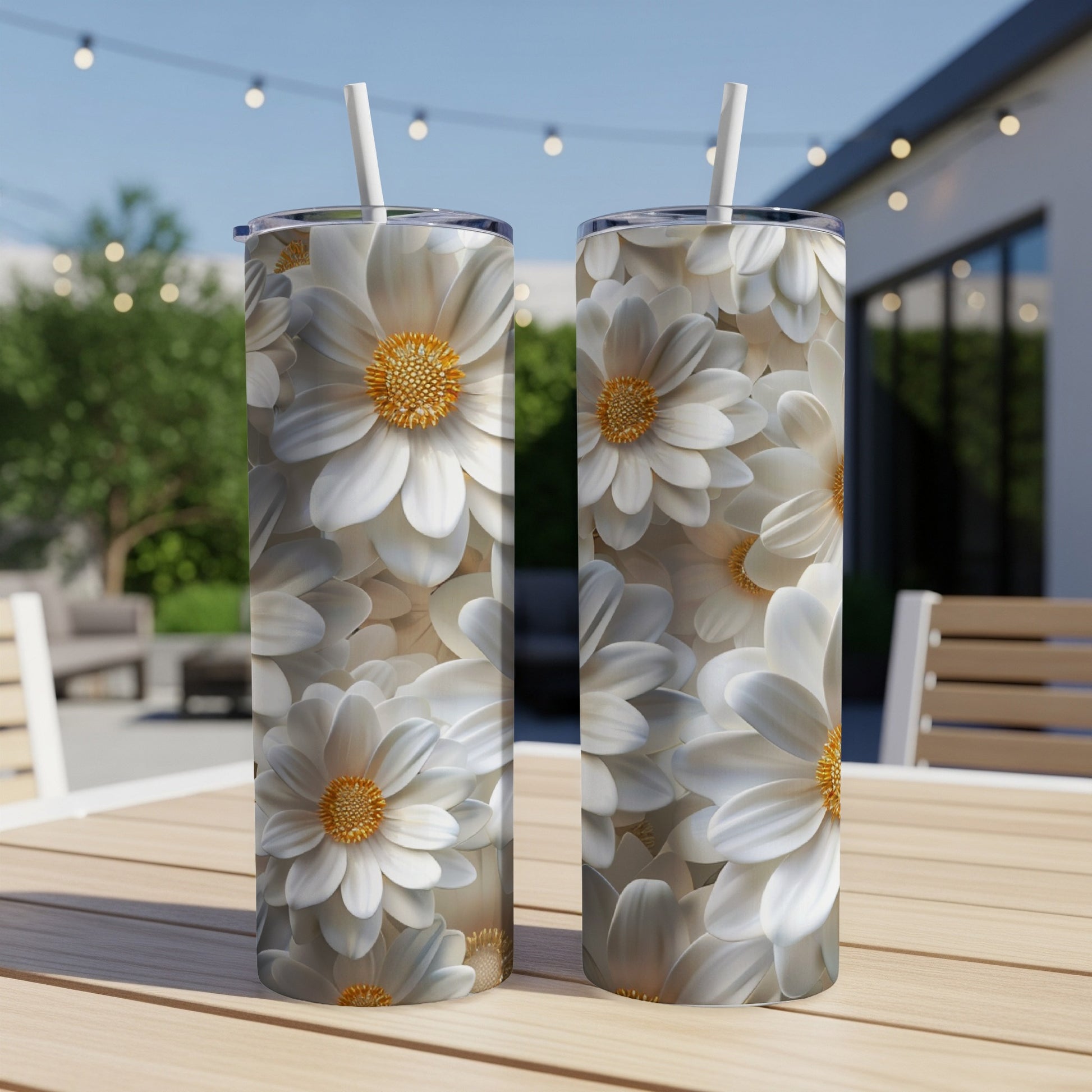Two white daisy patterned tumblers with straws on a wooden table.