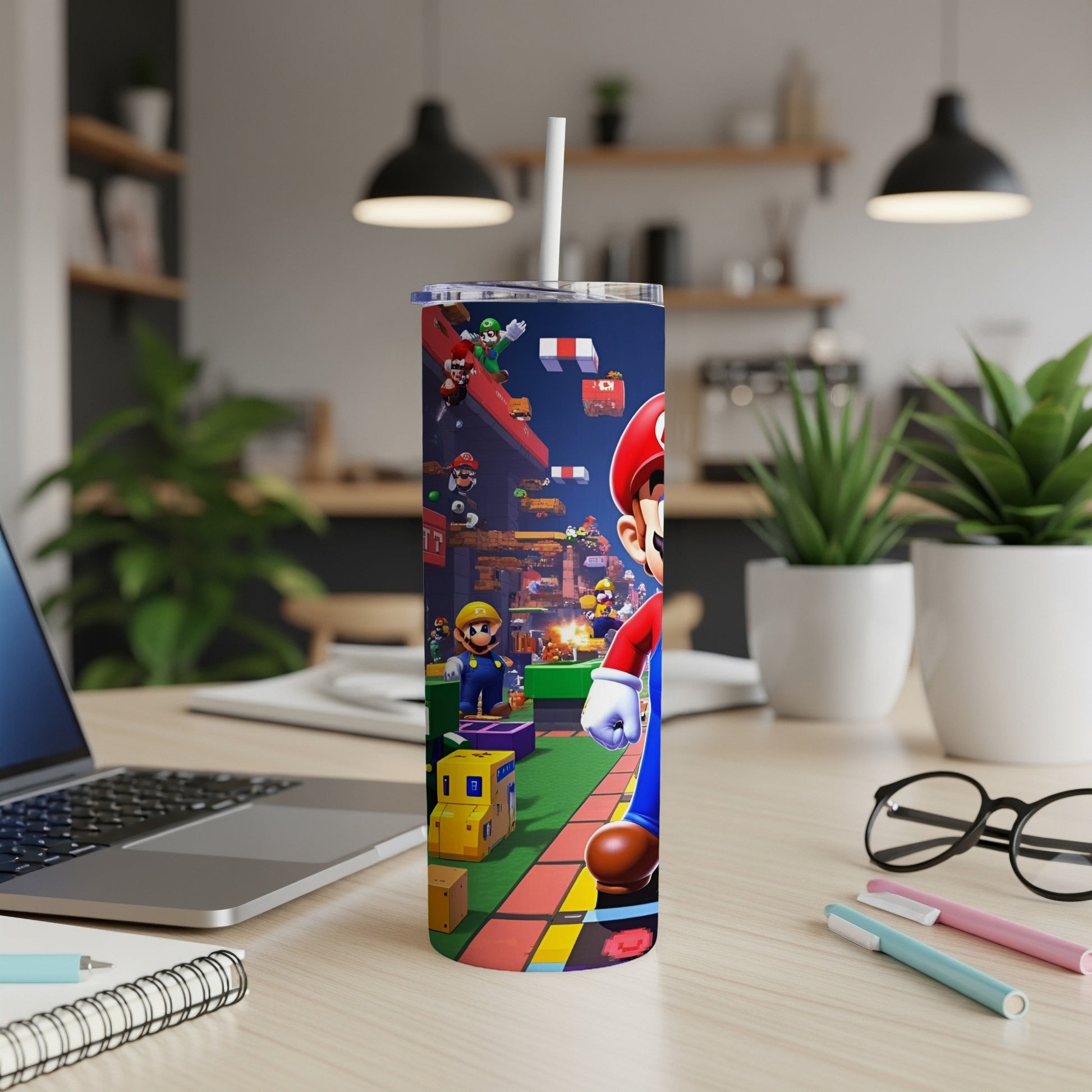 Super Mario characters on a skinny tumbler next to a laptop and pens.
