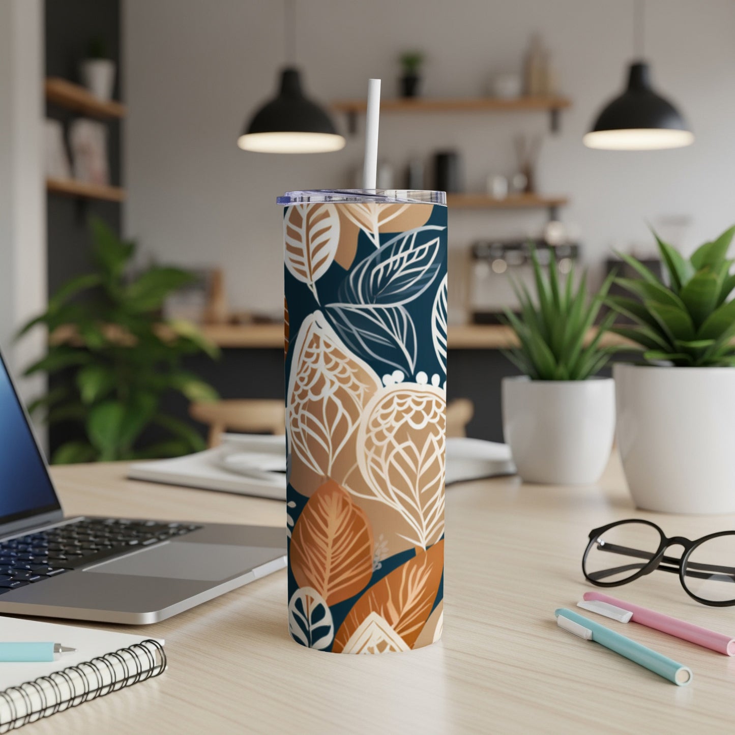 Floral patterned tumbler with straw on desk next to laptop and pens.