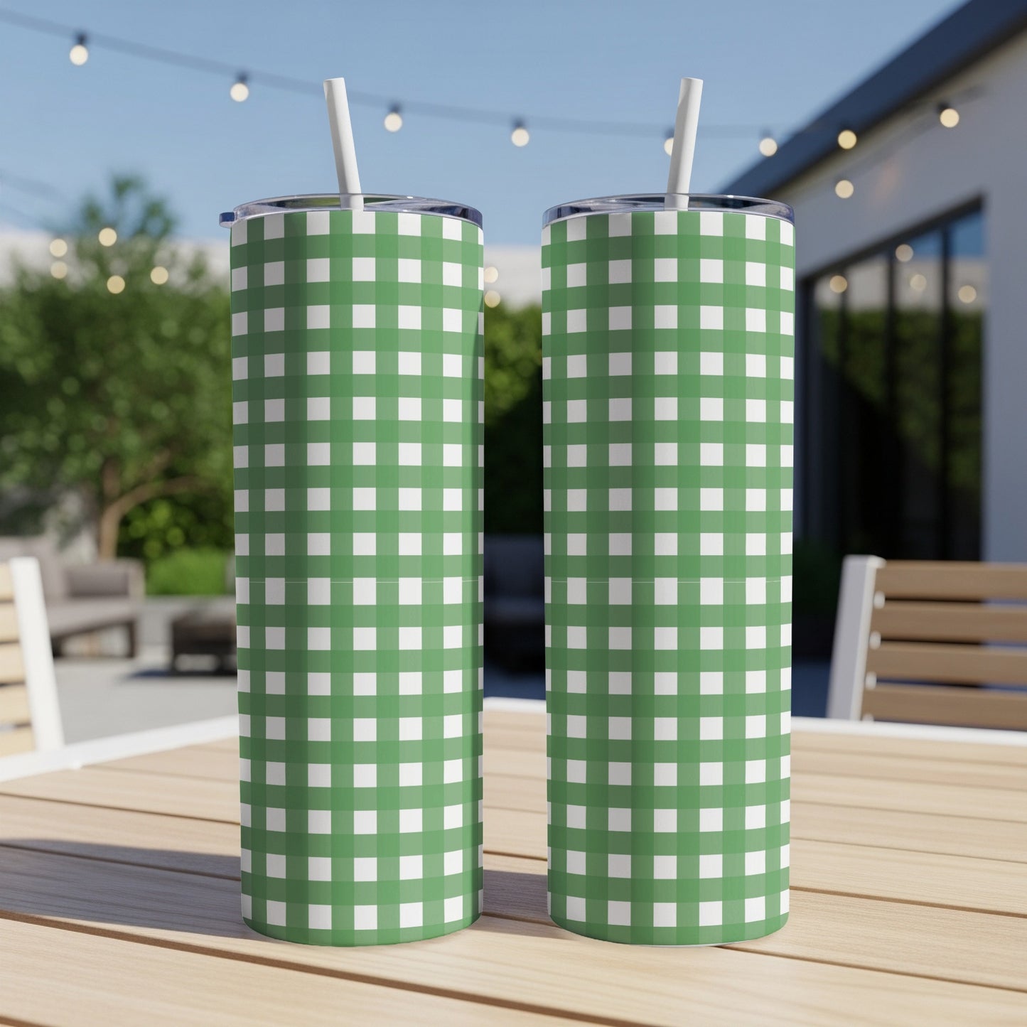 Two green and white gingham patterned tumblers with straws sit on a table.