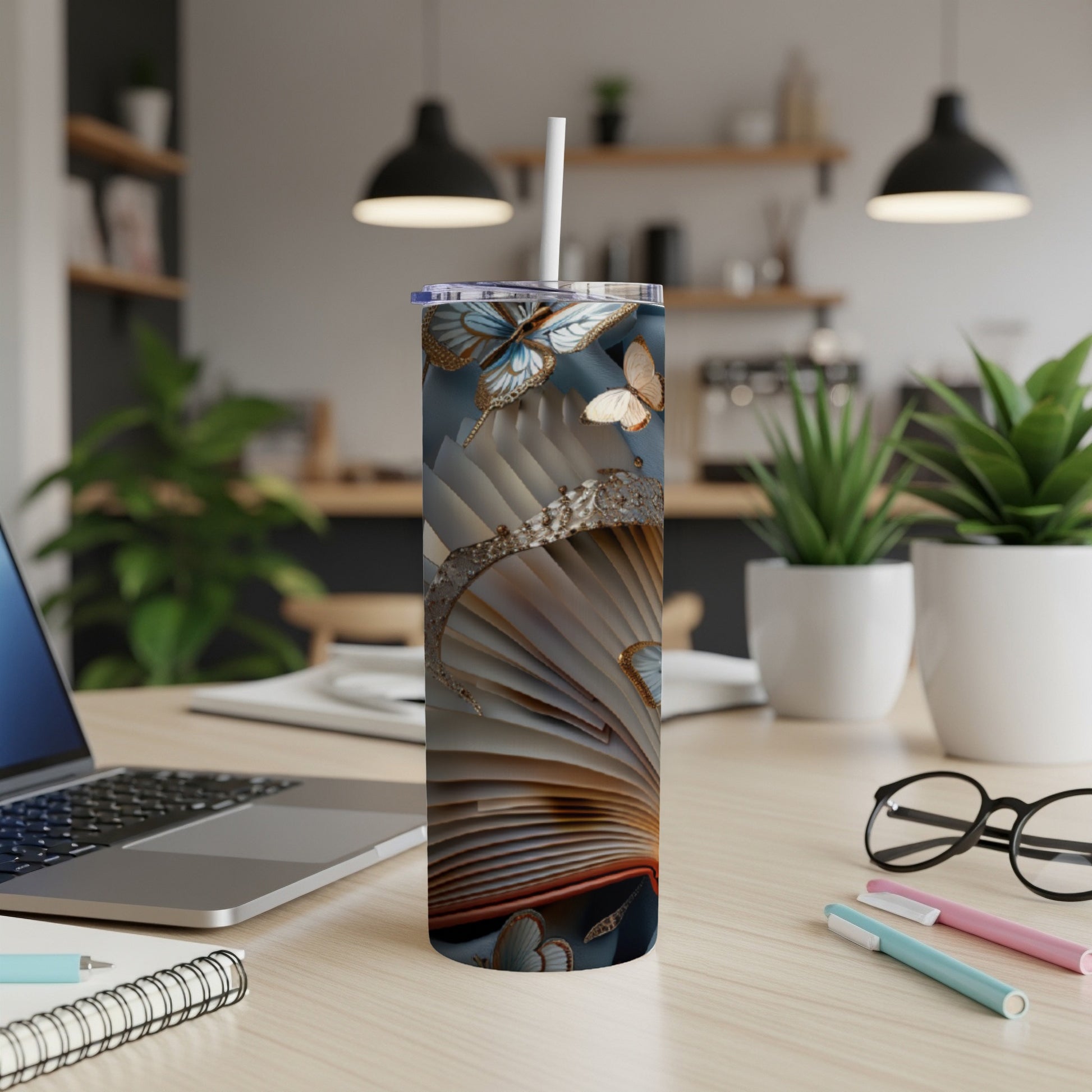 Tall tumbler with an open book and butterfly design, sitting on a desk.