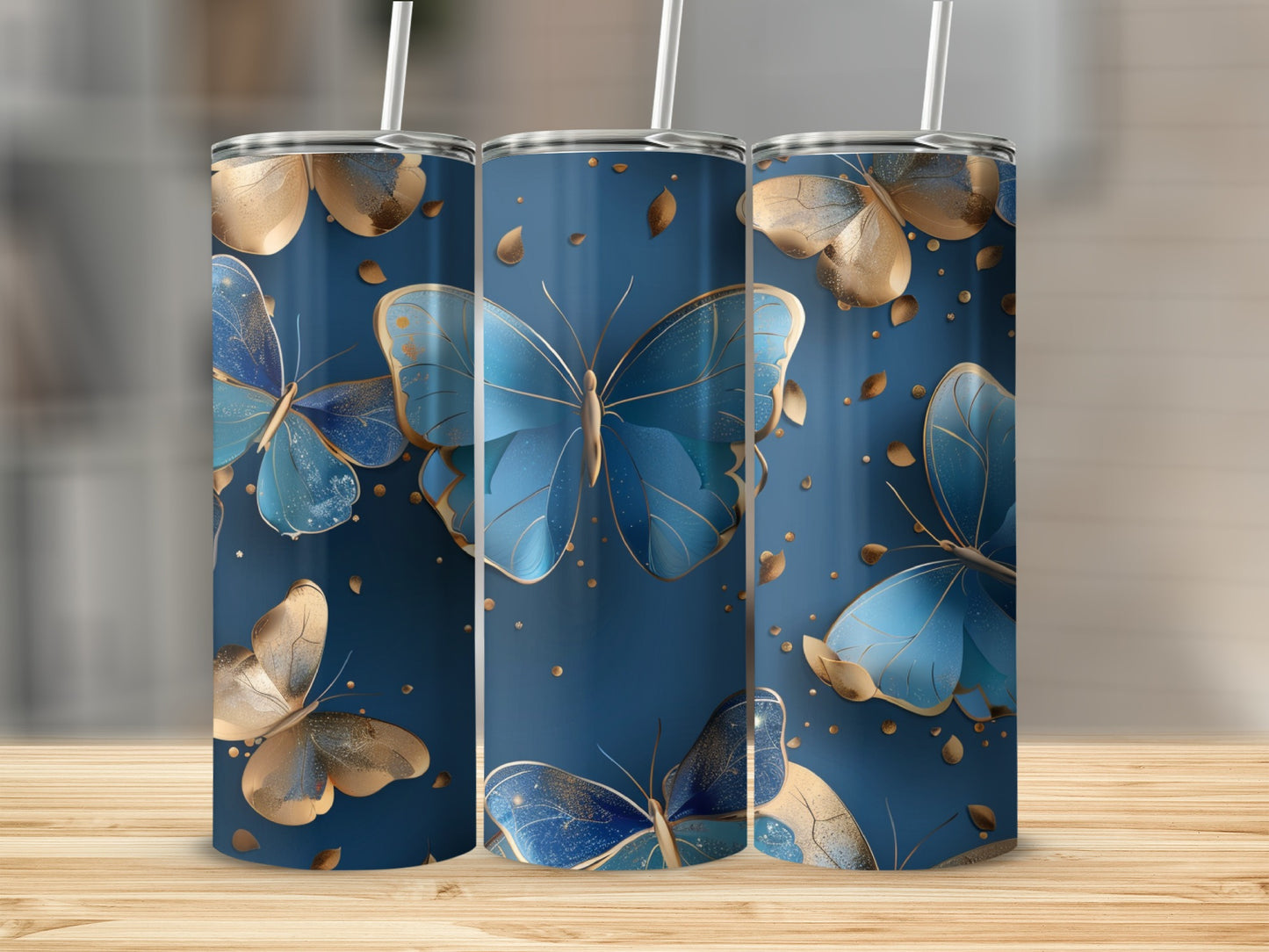 Three blue and gold butterfly tumblers with straws on a wooden surface.