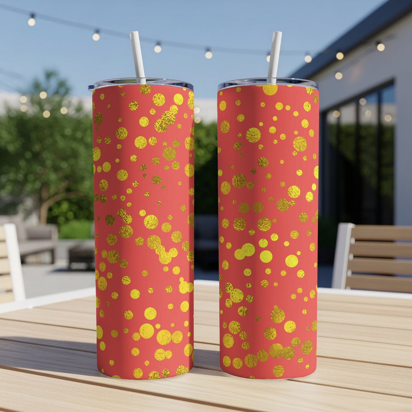 Two tumblers with a coral background and gold dot pattern, on a table outdoors.