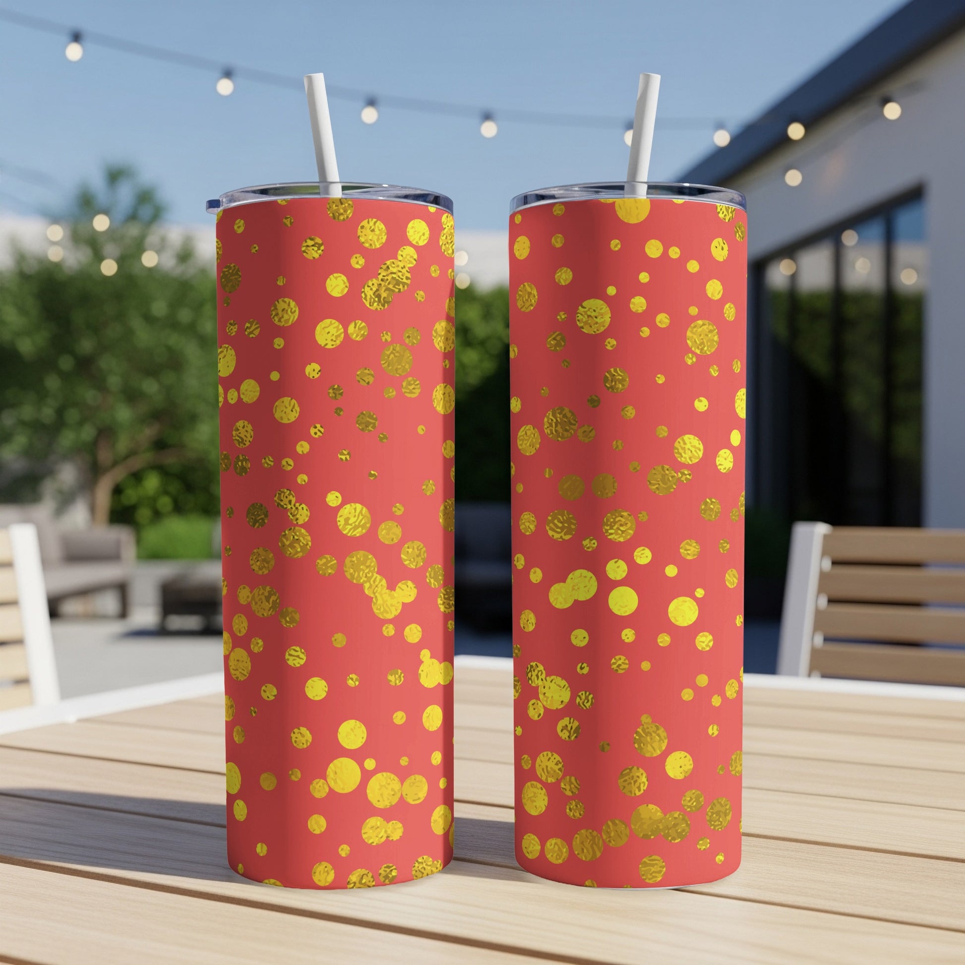 Two tumblers with a coral background and gold dot pattern, on a table outdoors.