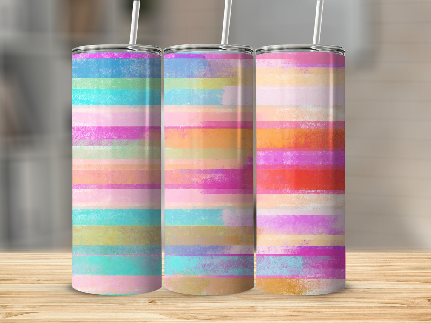Three tumblers with colorful horizontal stripe patterns displayed on a wooden surface.