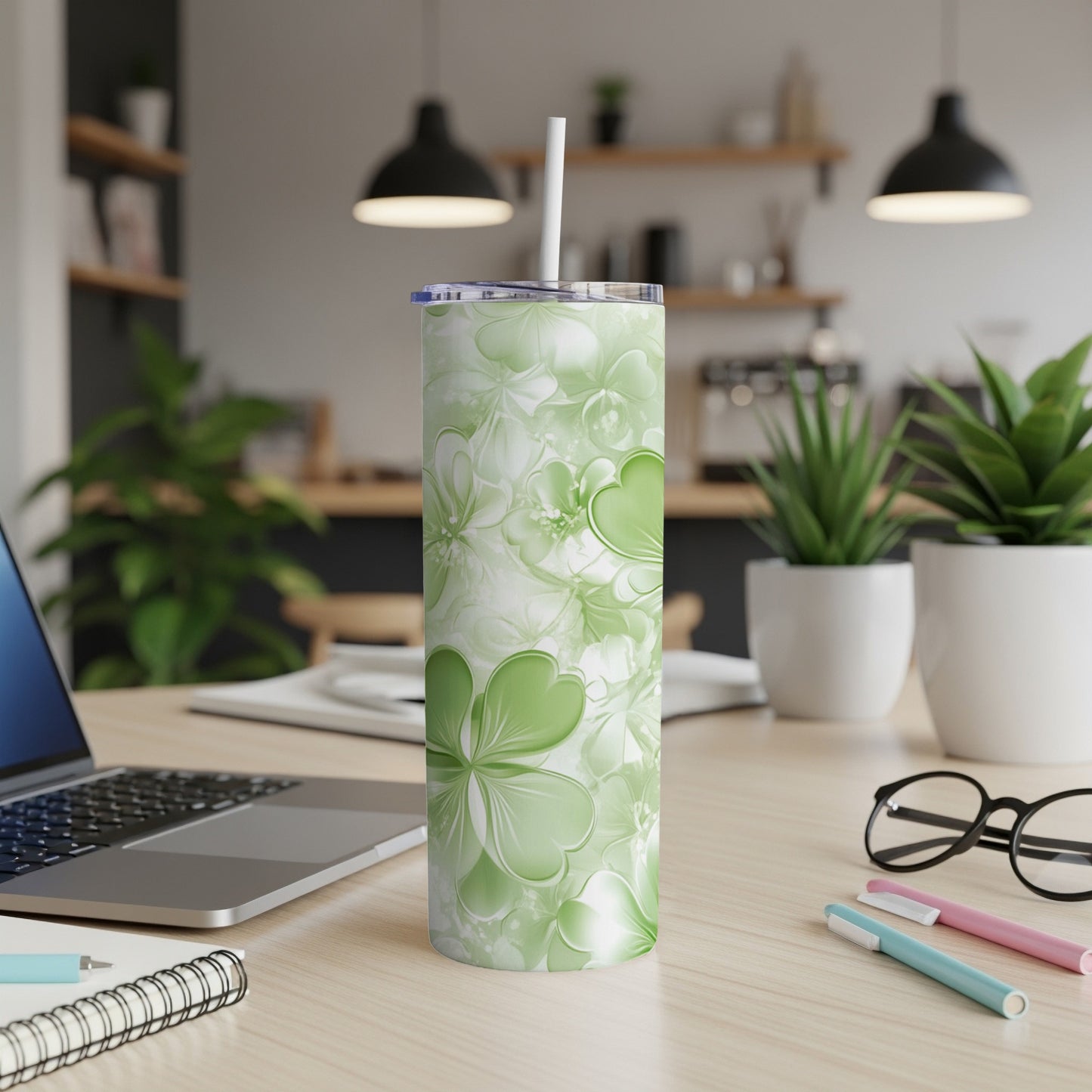 Green clover leaf and floral patterned tumbler with straw on desk.