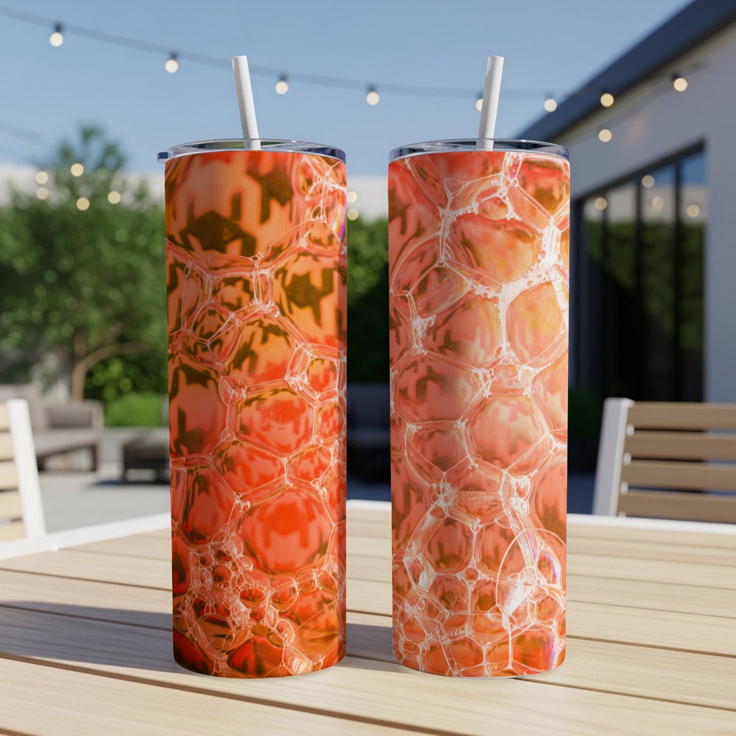 Two orange bubble pattern tumblers with straws on a wooden table outdoors.