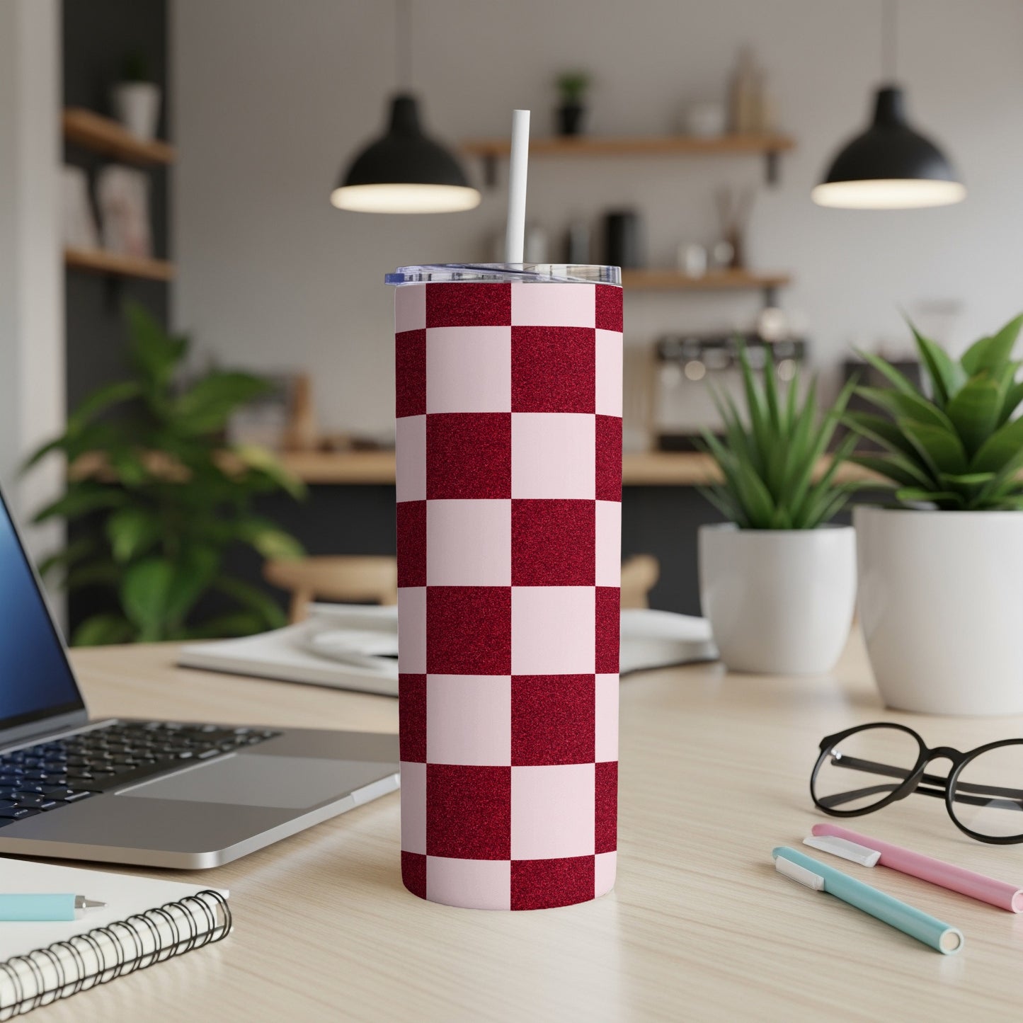 Red and pink checkered tumbler with a straw on a desk.