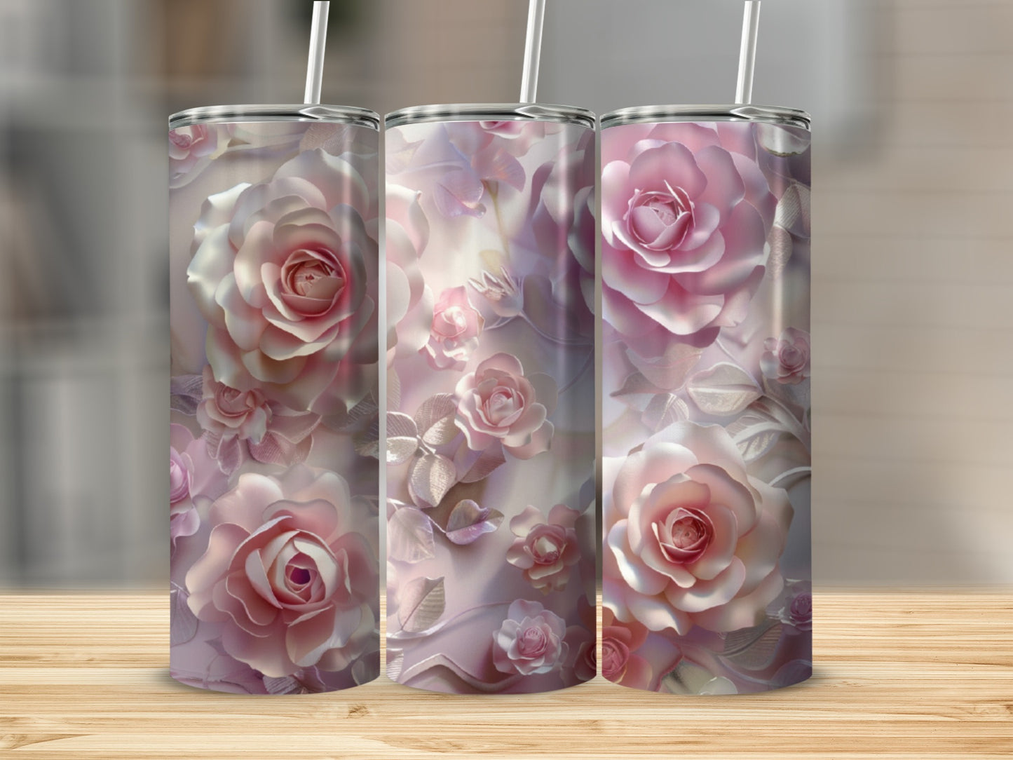 Three pink rose print tumblers with straws on a wooden surface.