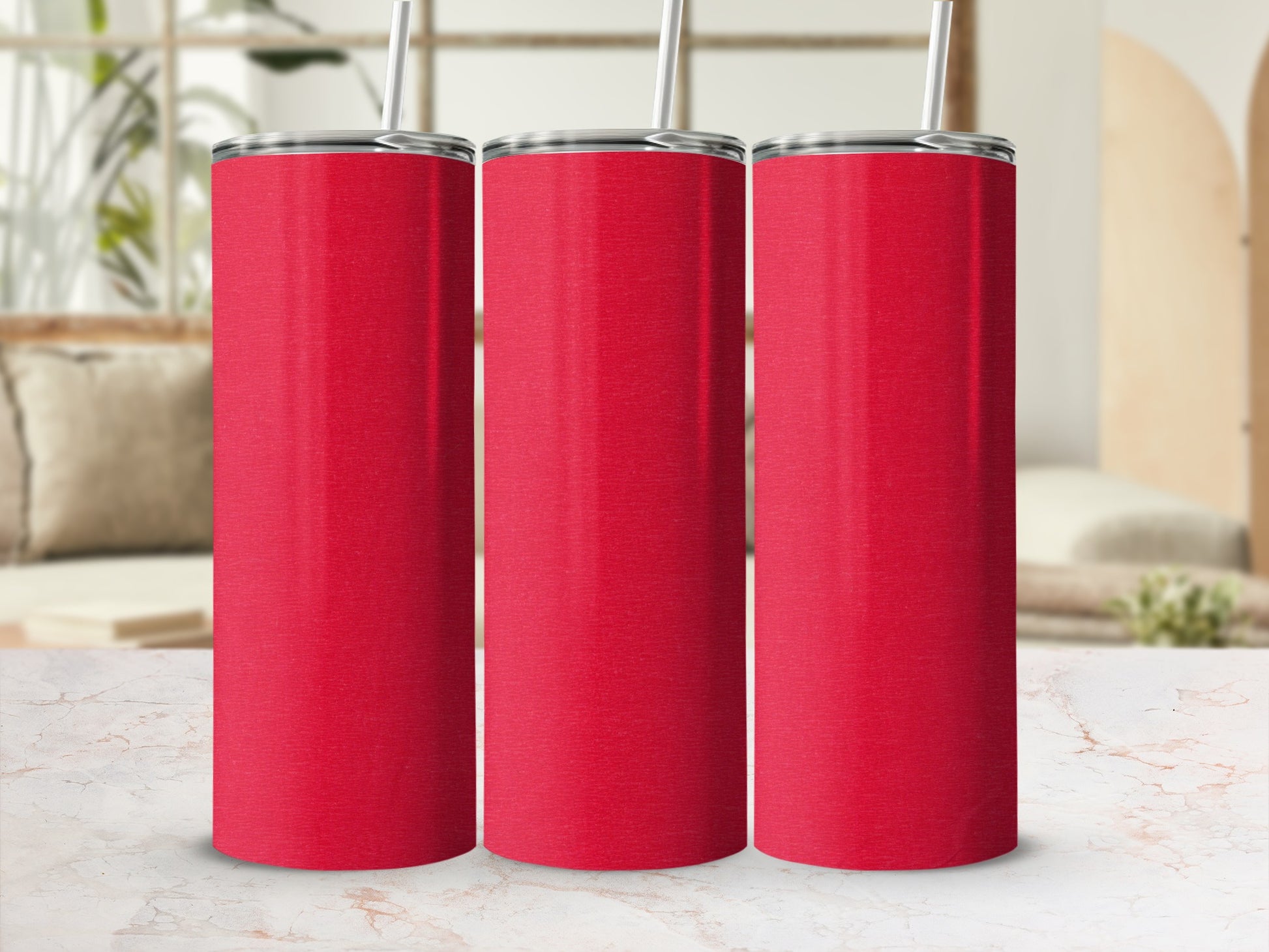 Three red stainless steel tumblers with straws sit on a marble surface.