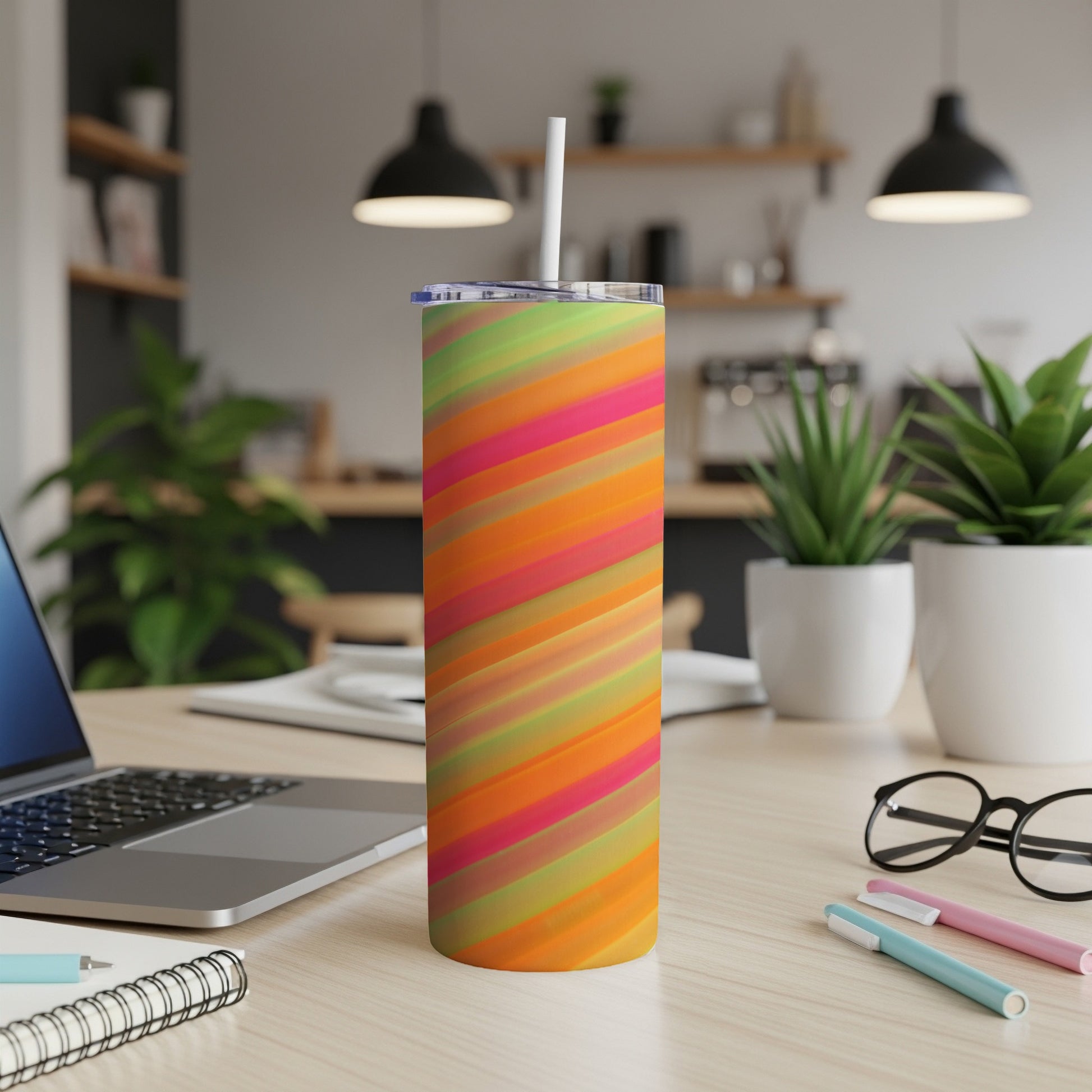 Colorful striped tumbler with straw on a desk next to a laptop.