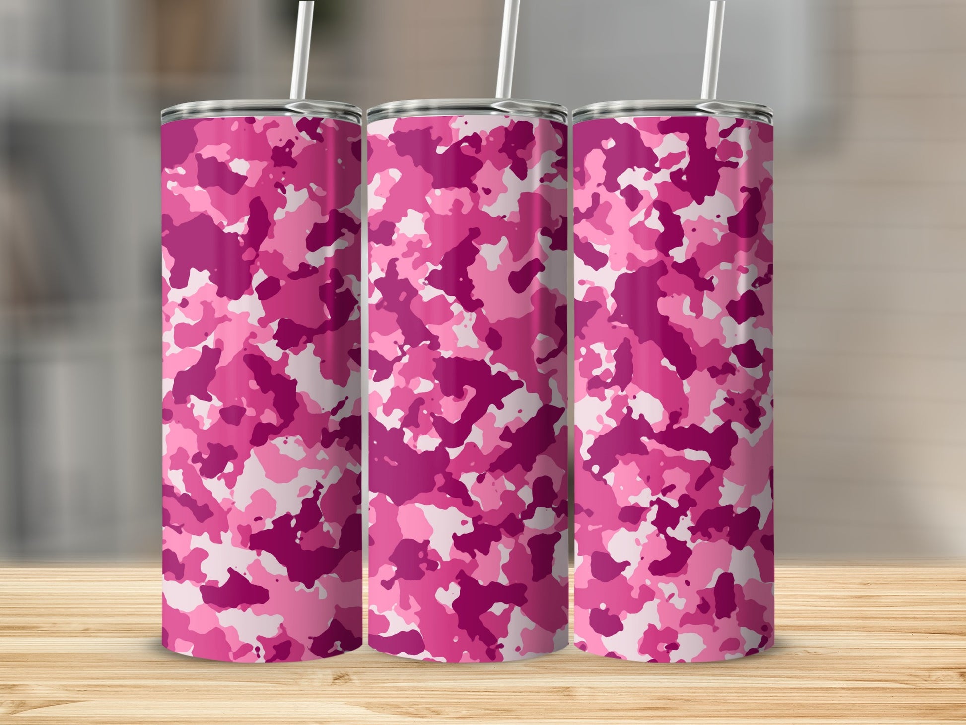 Three pink camouflage tumblers with white straws on a wooden surface.