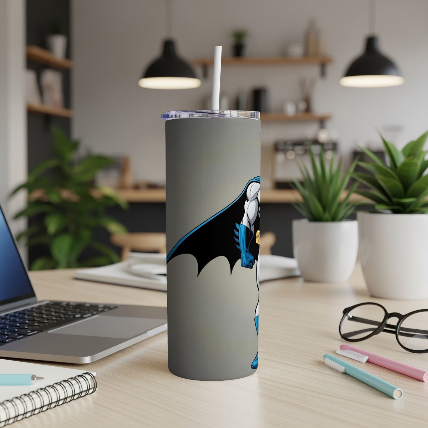 Batman graphic on a grey tumbler with a straw, on a desk.