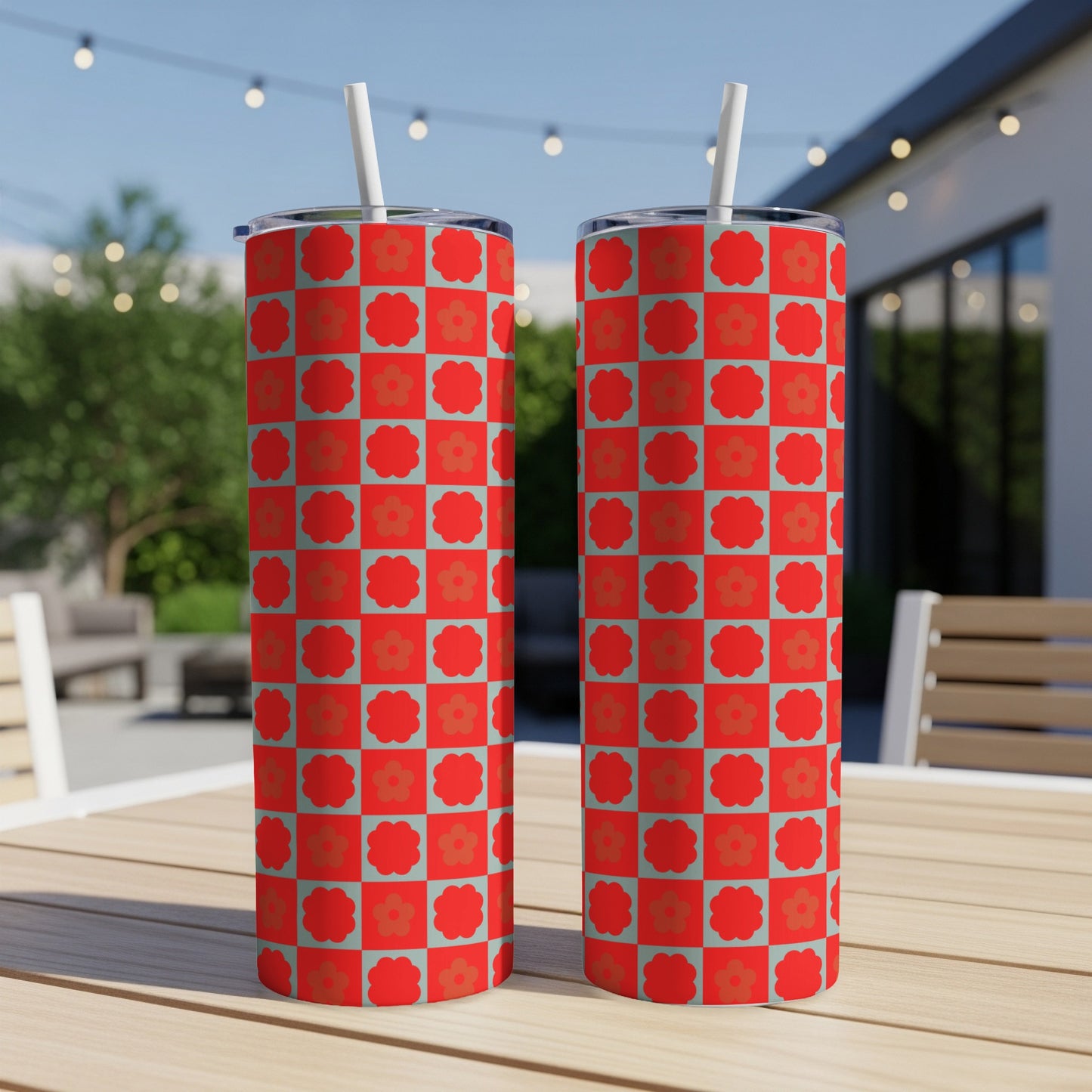 Two red and teal floral checkered pattern tumblers with straws on a wooden table.