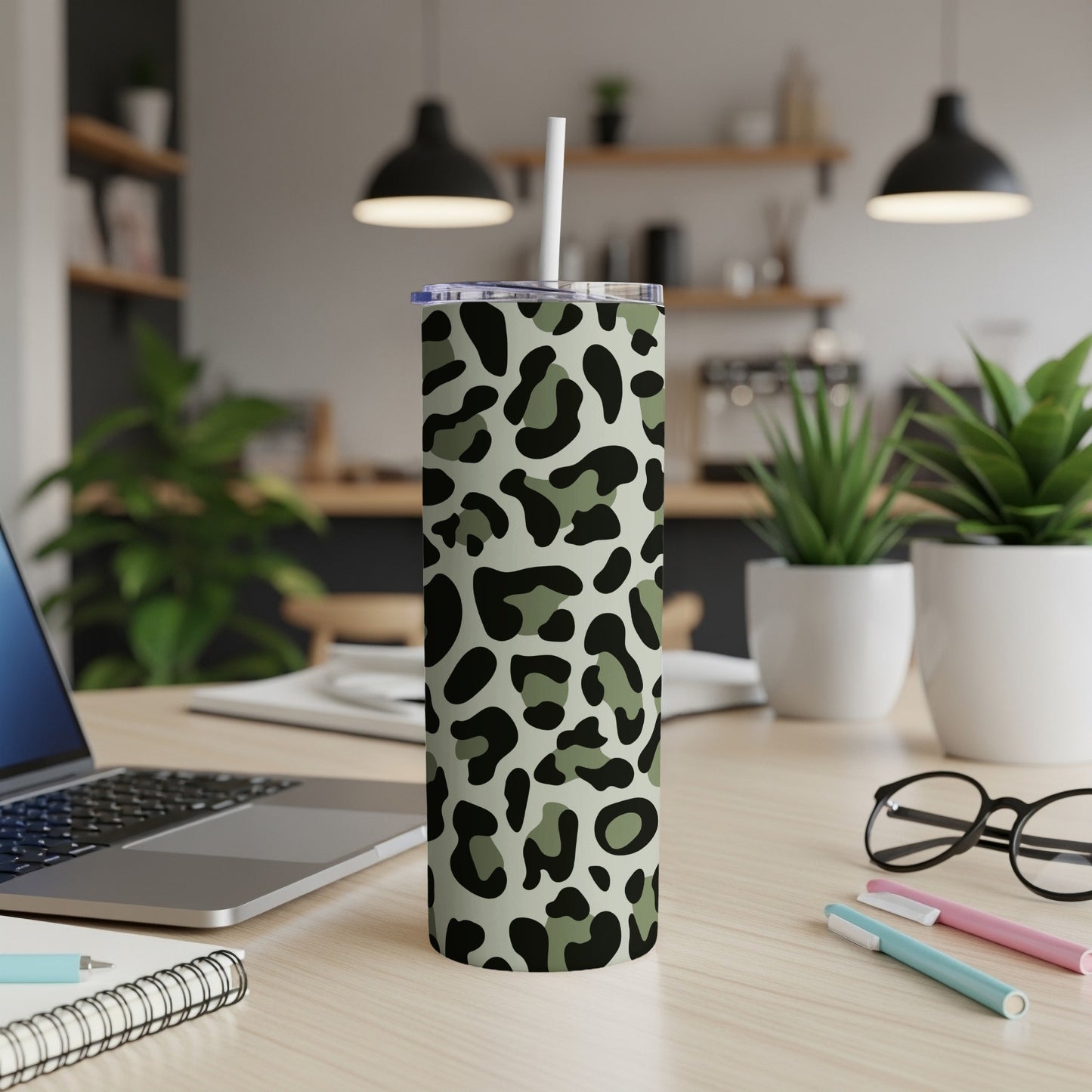 Camouflage leopard print tumbler with straw on a desk with laptop and plants.