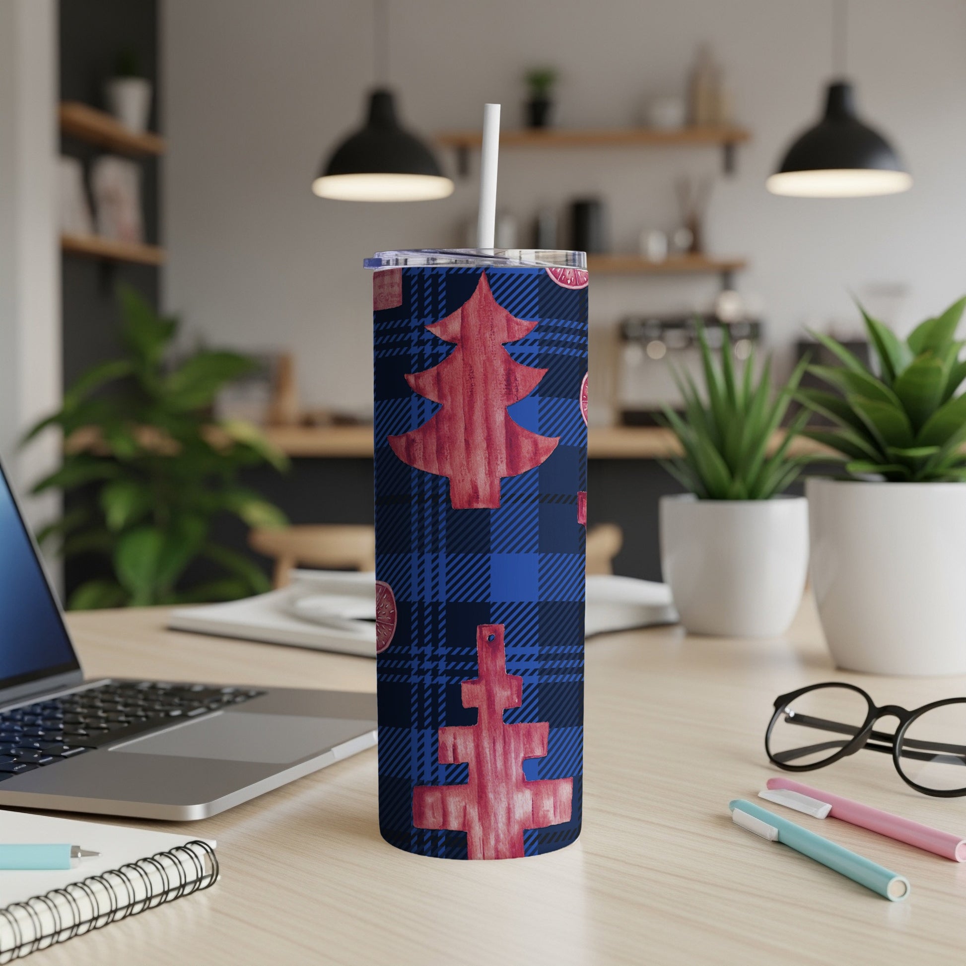 Blue plaid tumbler with red Christmas trees and citrus slices, on a desk.