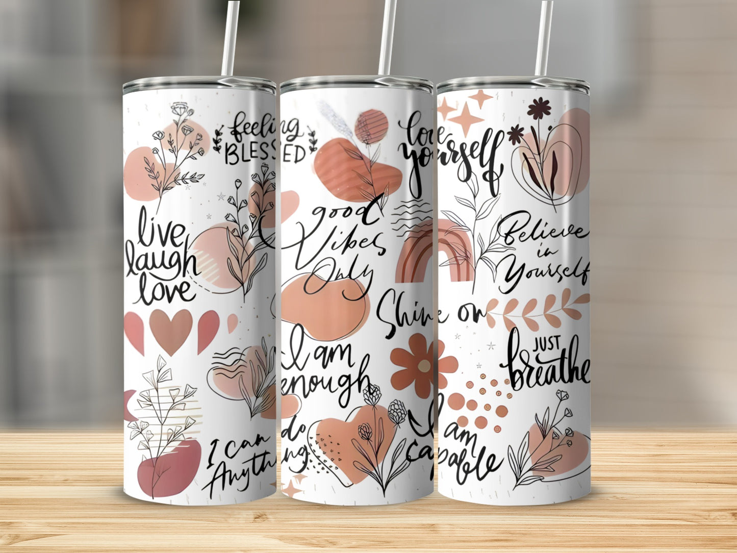 Three tumblers with inspirational text and floral line art on a wooden surface.