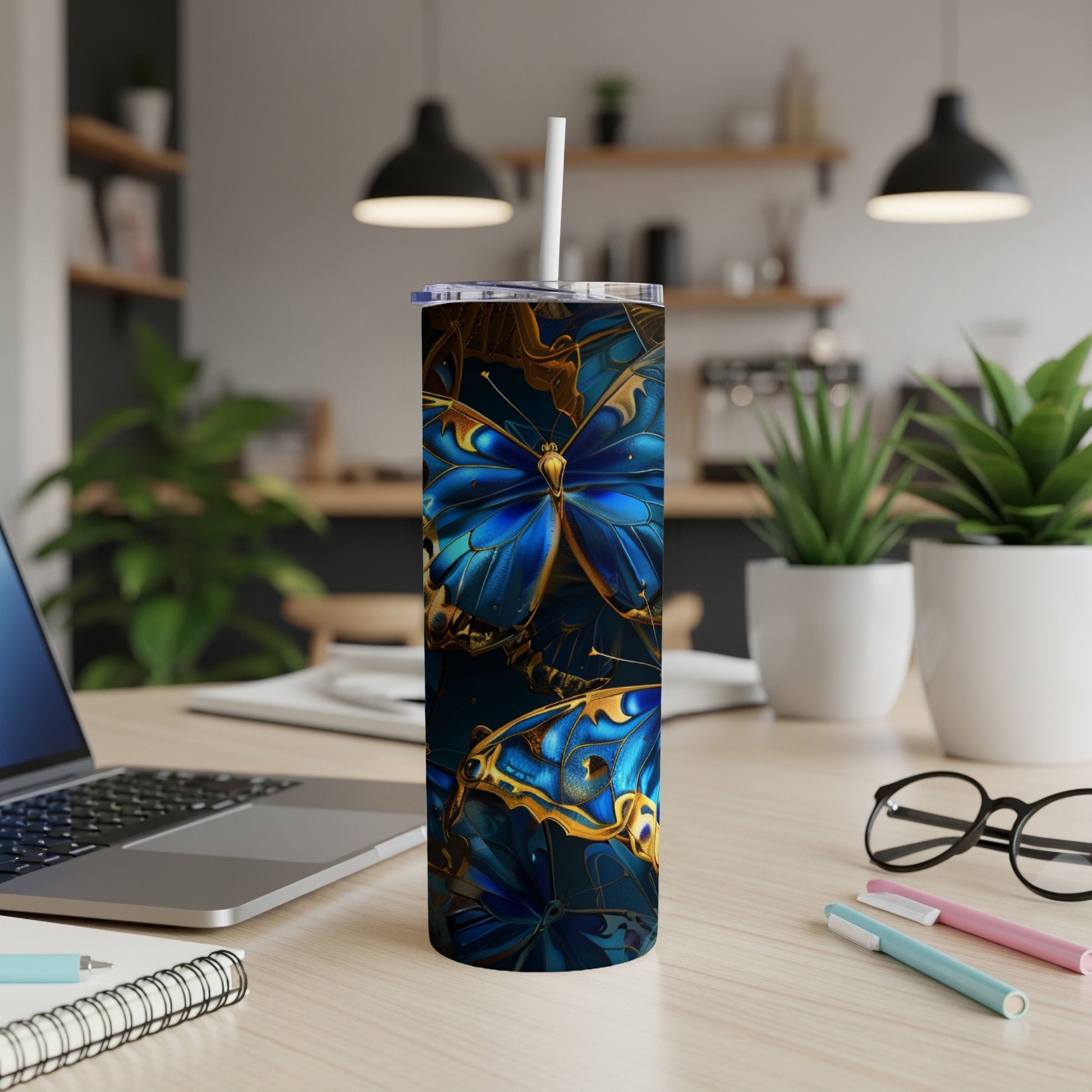 Blue and gold butterfly patterned tumbler with straw on a desk.