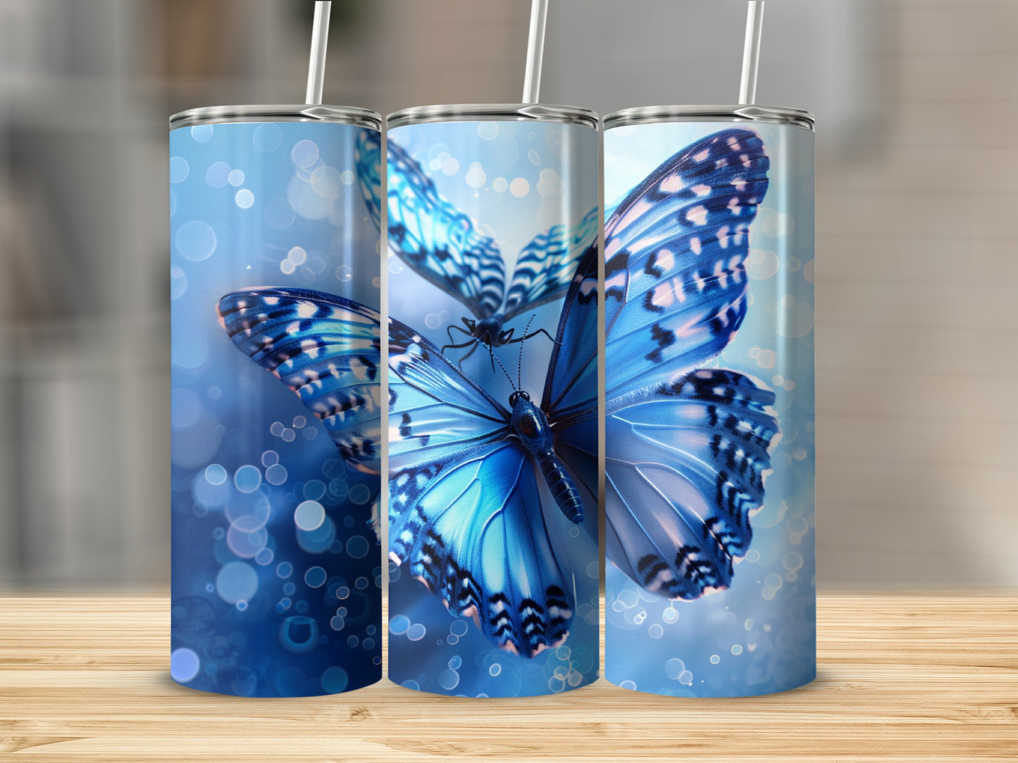 Three tumblers with blue butterflies and bokeh effect on wooden surface.