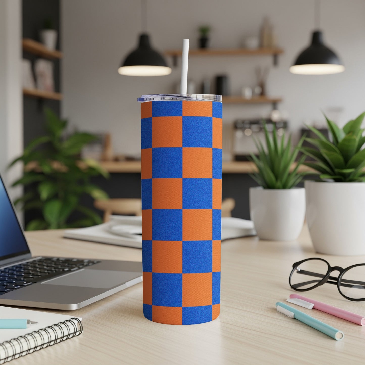 Orange and blue checkered tumbler with a straw, on a desk.