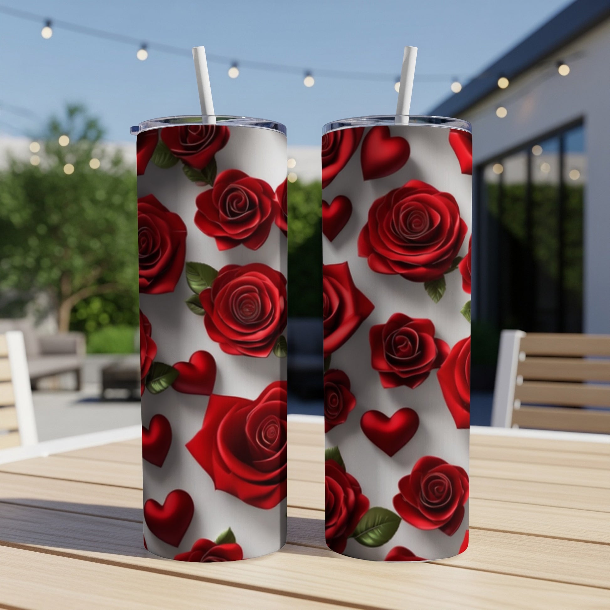 Two tumblers with red roses and hearts pattern on a wooden table outdoors.