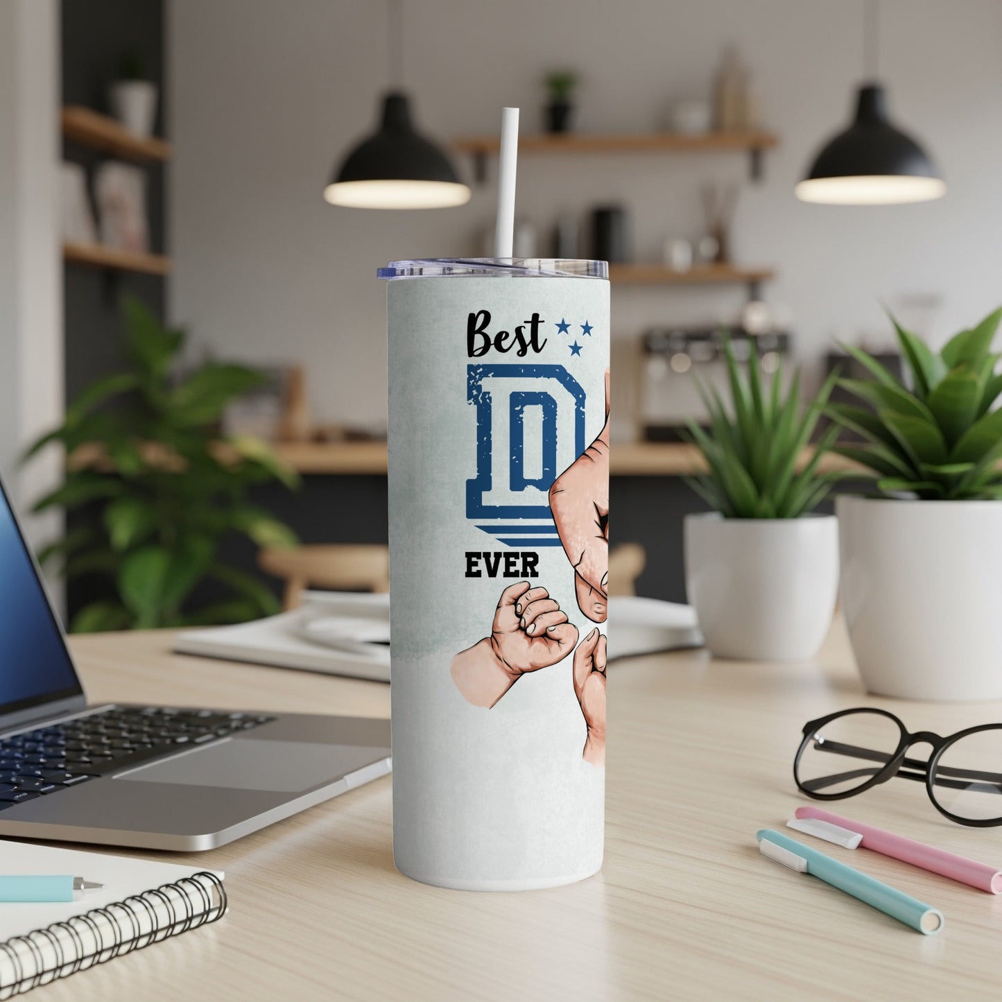 White tumbler with text "Best D EVER" and hand graphics, on a desk.