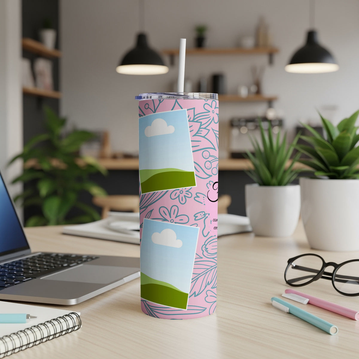 Pink tumbler with floral pattern and two photo frames, on a desk.