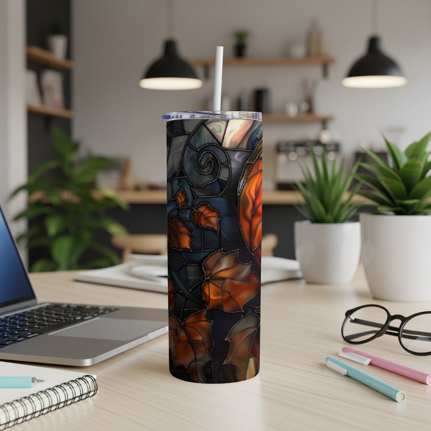 Stained glass tumbler with autumn leaves design on a desk.