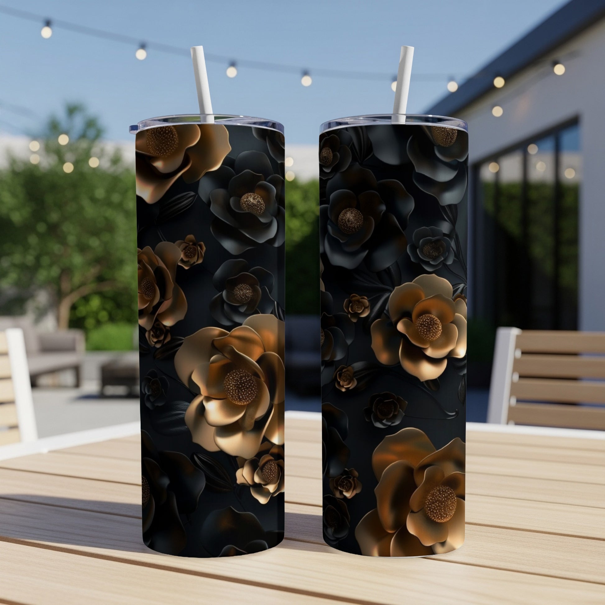 Two black tumblers with raised gold floral patterns on a wooden table outdoors.