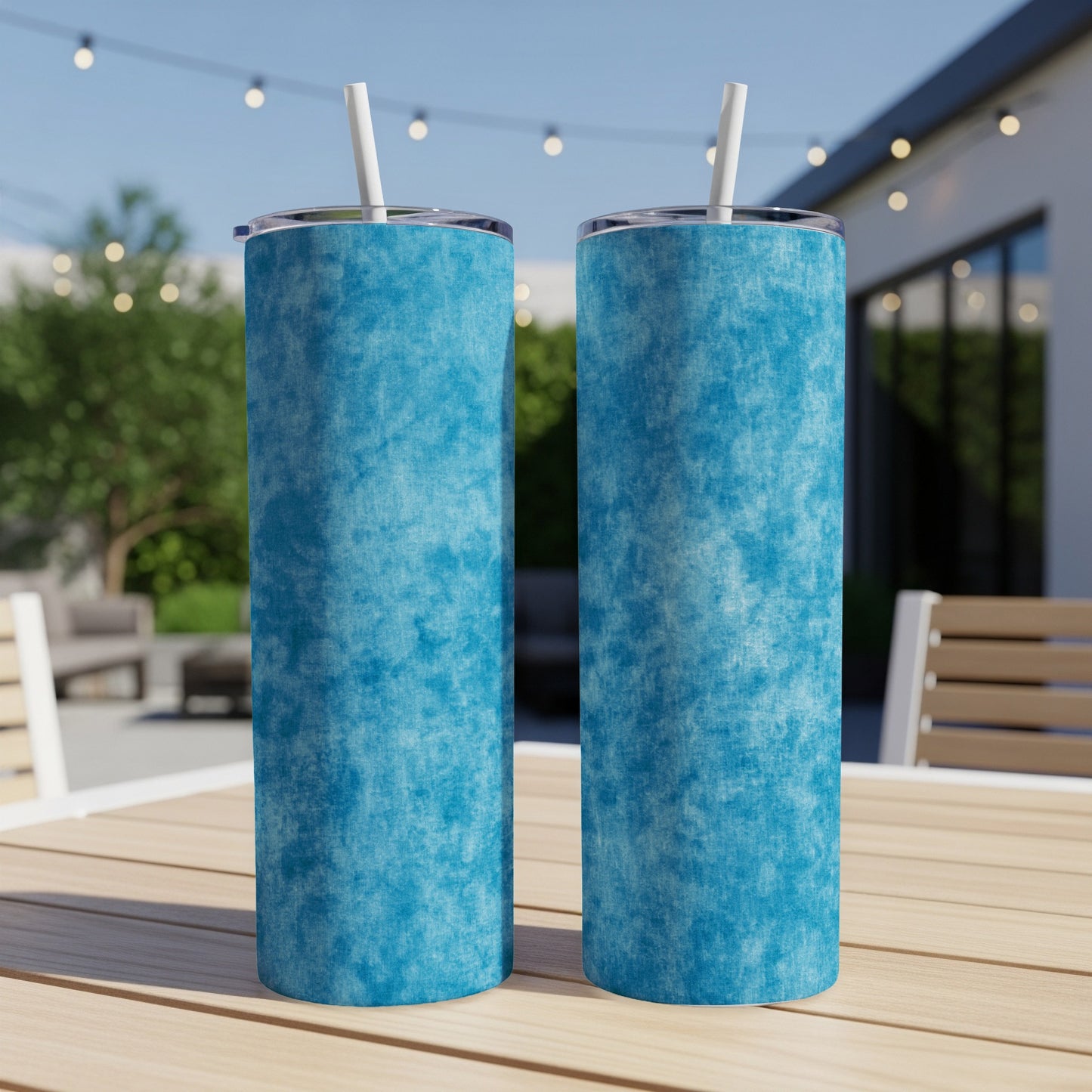 Two blue textured tumblers with white straws sit on a wooden table outdoors.