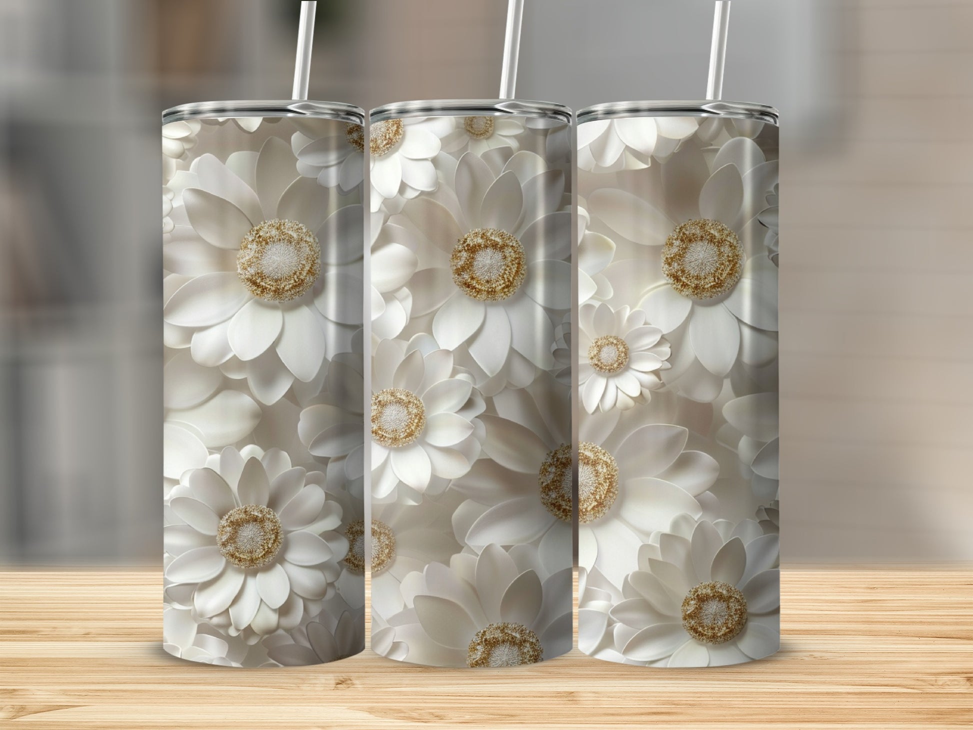 Three white floral tumblers with gold centers and straws on a wooden surface.