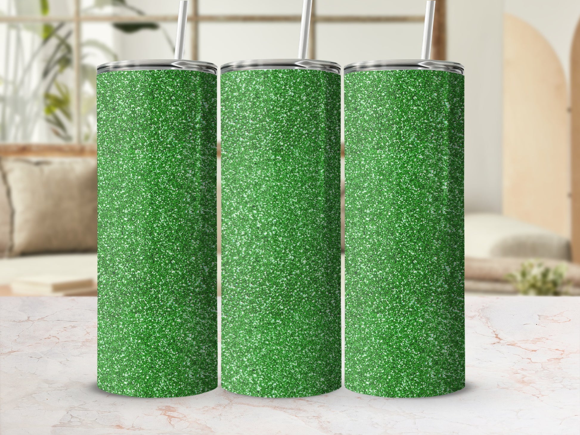 Three green glitter tumblers with silver lids and straws on a marble surface.