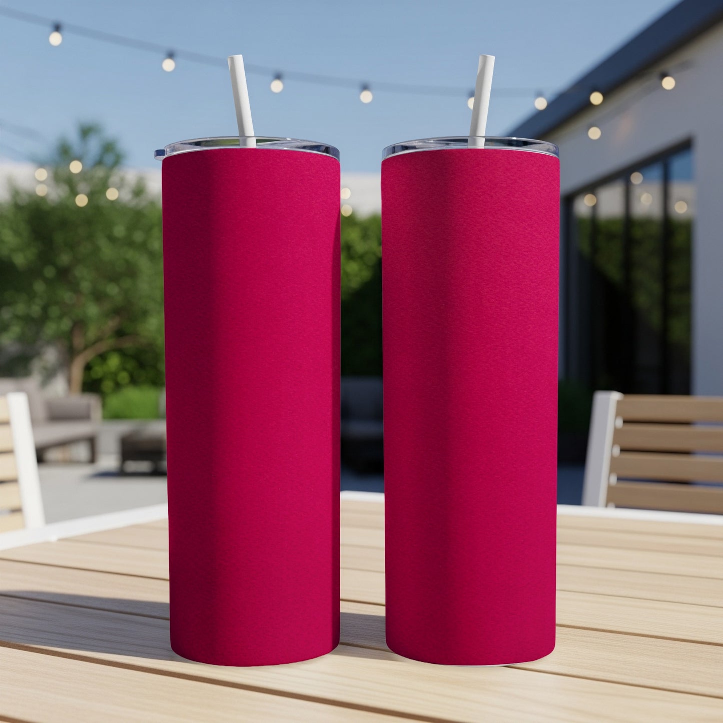 Two magenta tumblers with white straws sit on a wooden table outdoors.