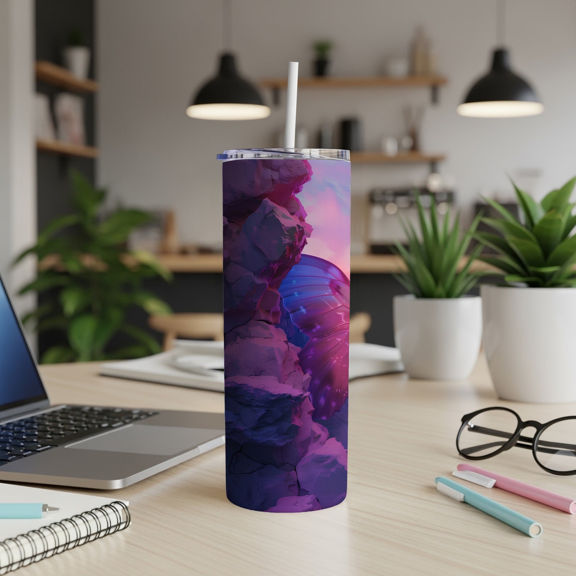 Tumbler with butterfly wing design on desk next to laptop and pens.