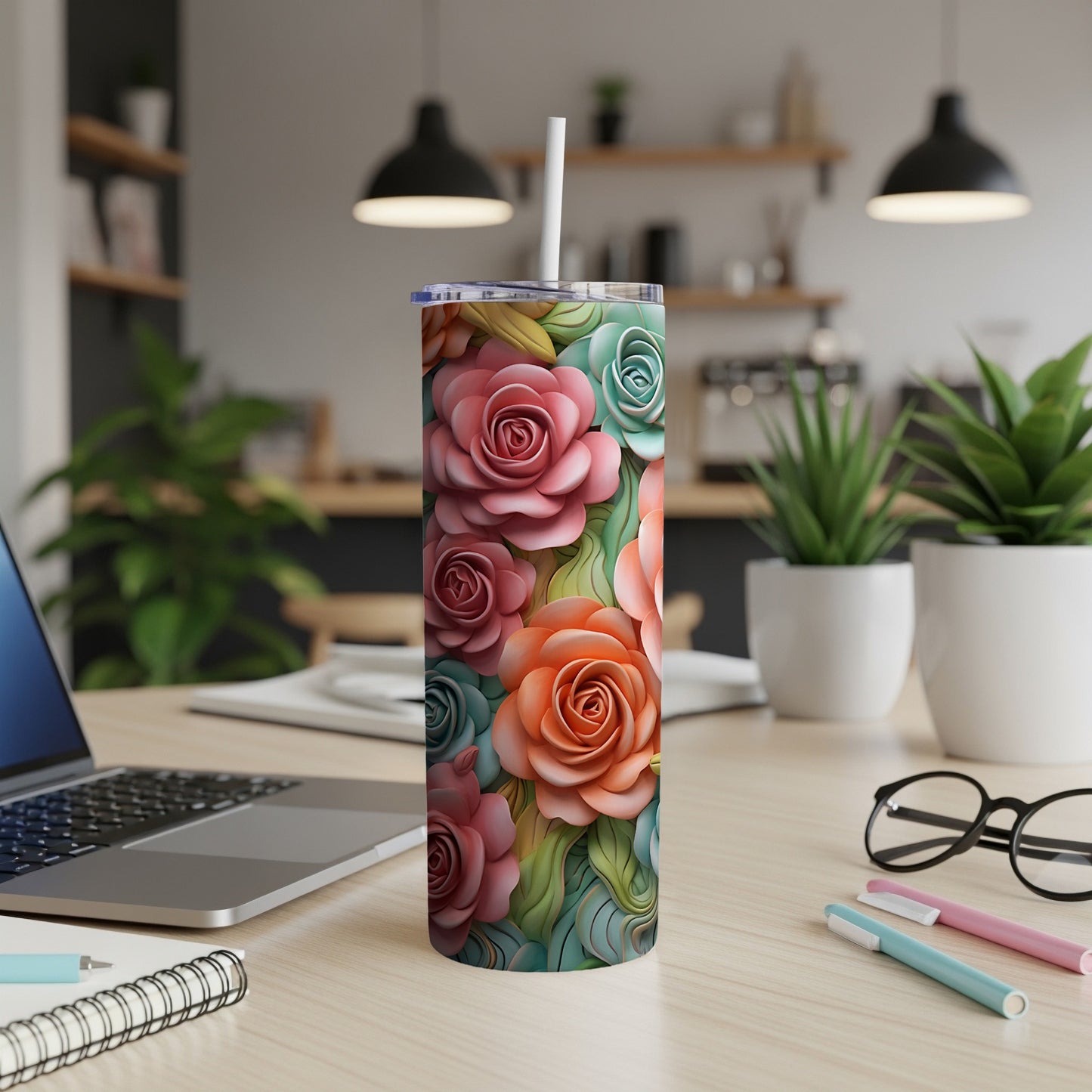 Floral tumbler with roses and leaves on a desk with a laptop.