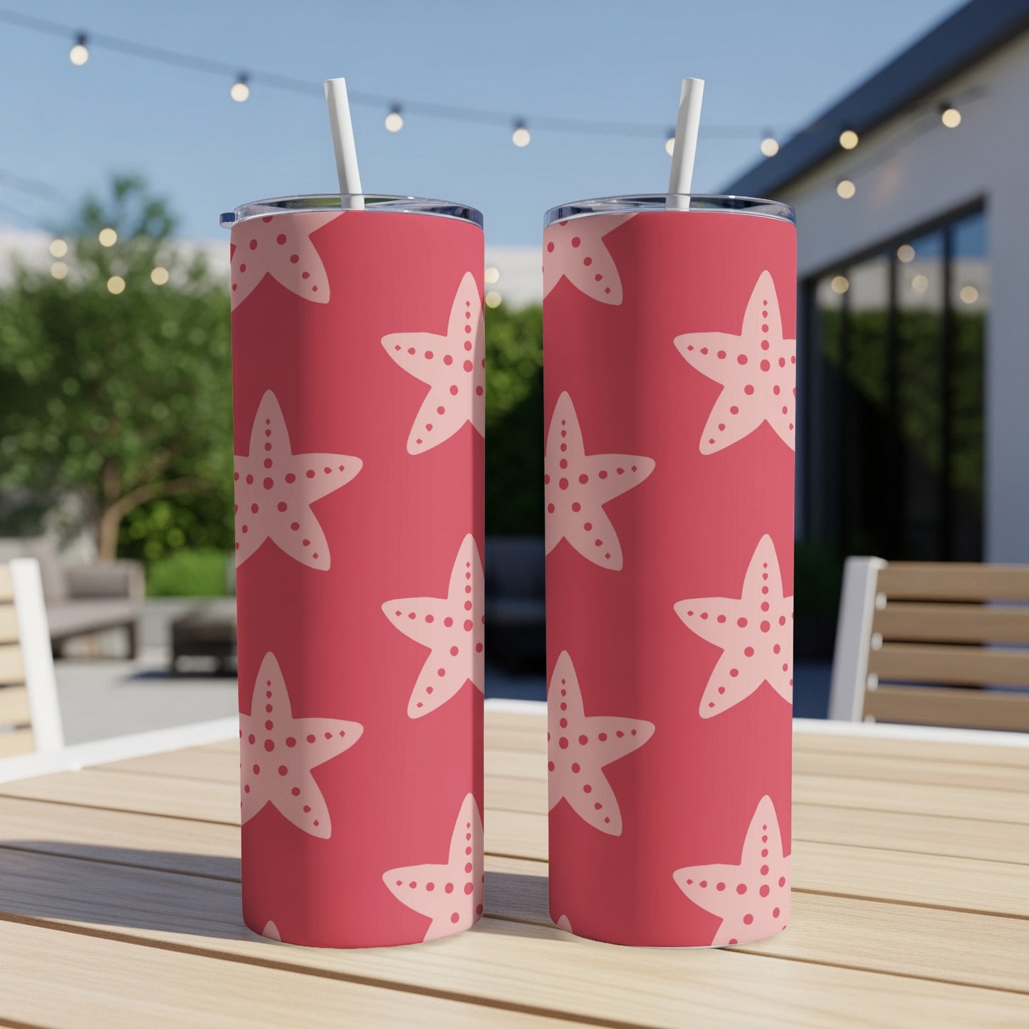 Two pink tumblers with white starfish pattern on a wooden table.