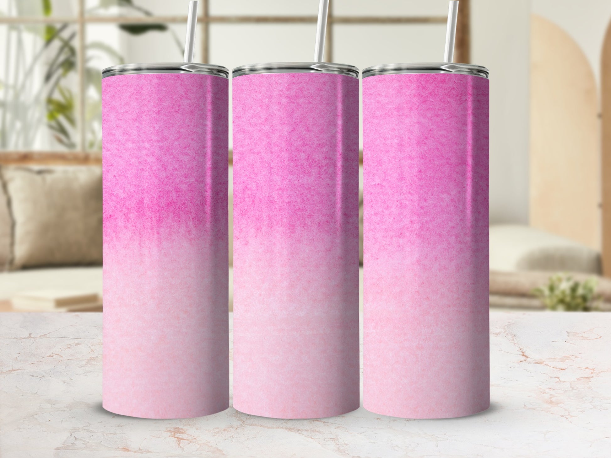 Three pink ombre tumblers with straws on a marble surface.