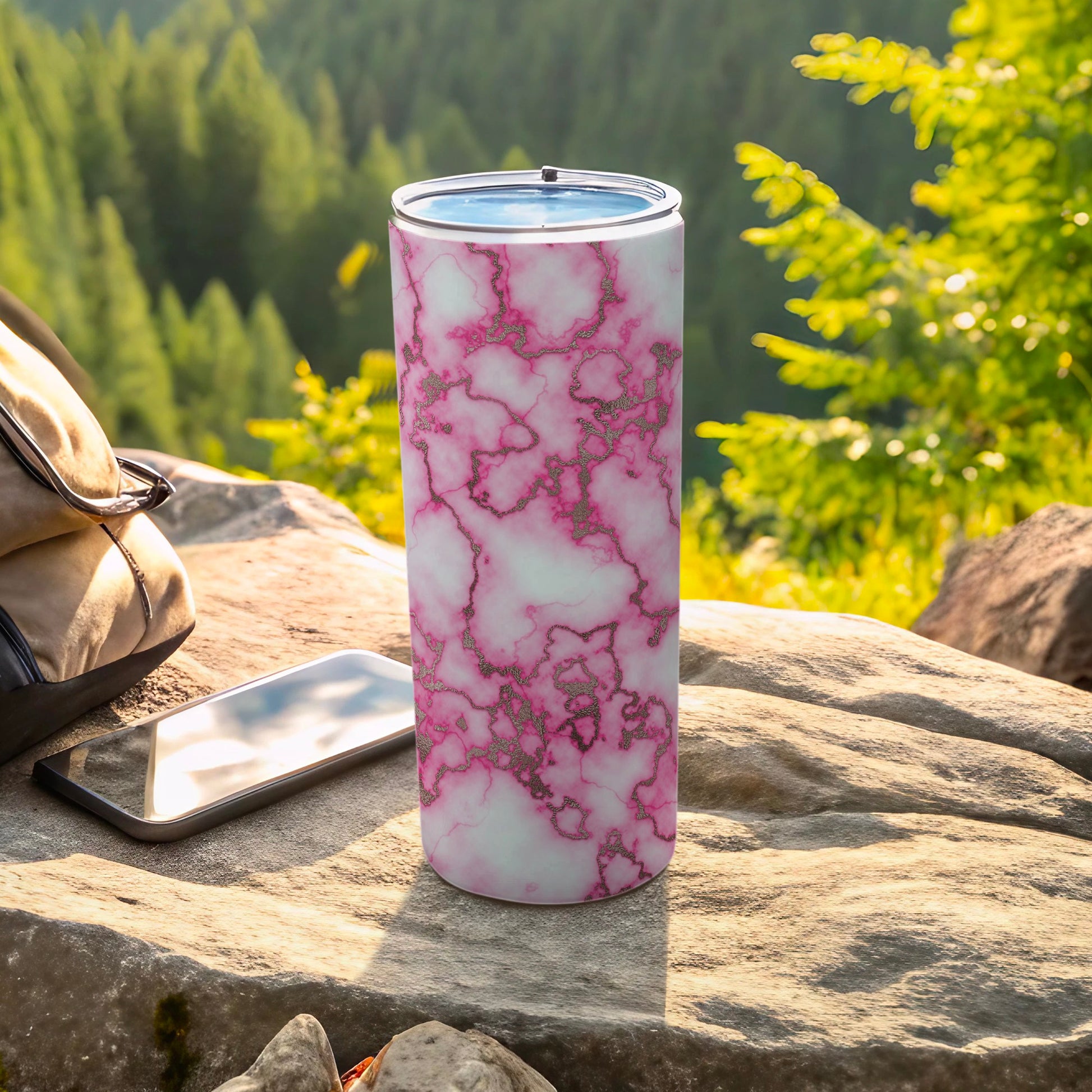Marble tumbler with pink veins on a rock next to a phone and backpack.