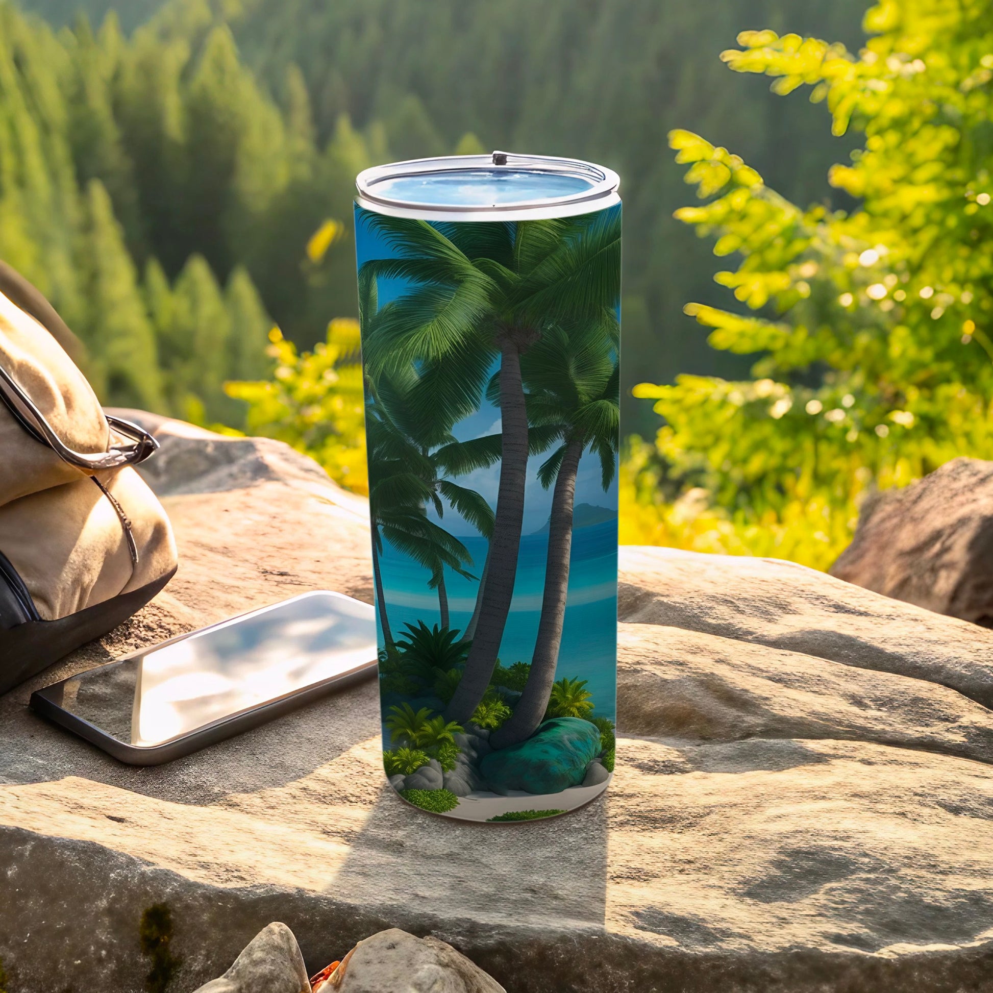 Tall tumbler with palm trees and ocean design, on a rock with a phone.