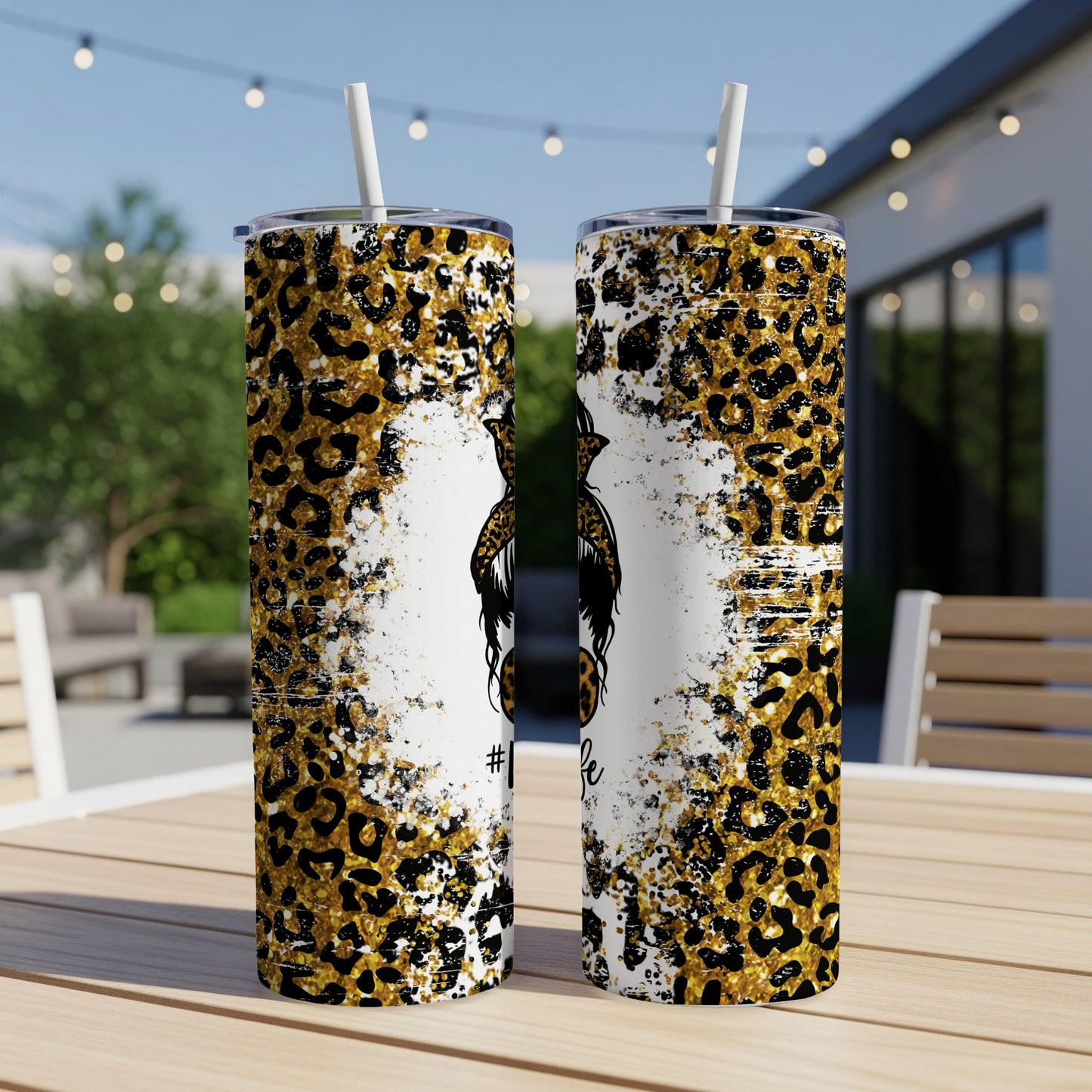 Two leopard print tumblers with black messy bun graphic on wooden table outdoors.