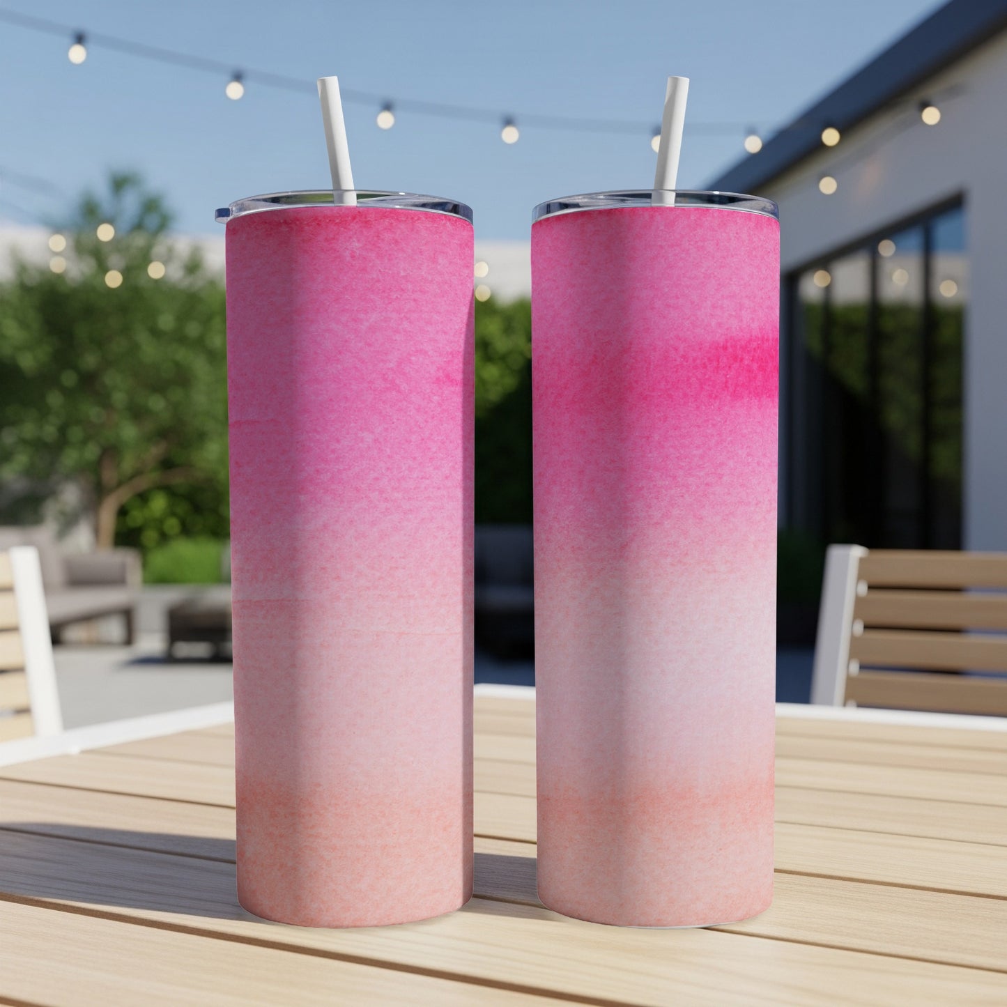 Two pink ombre tumblers with straws sit on a wooden table.