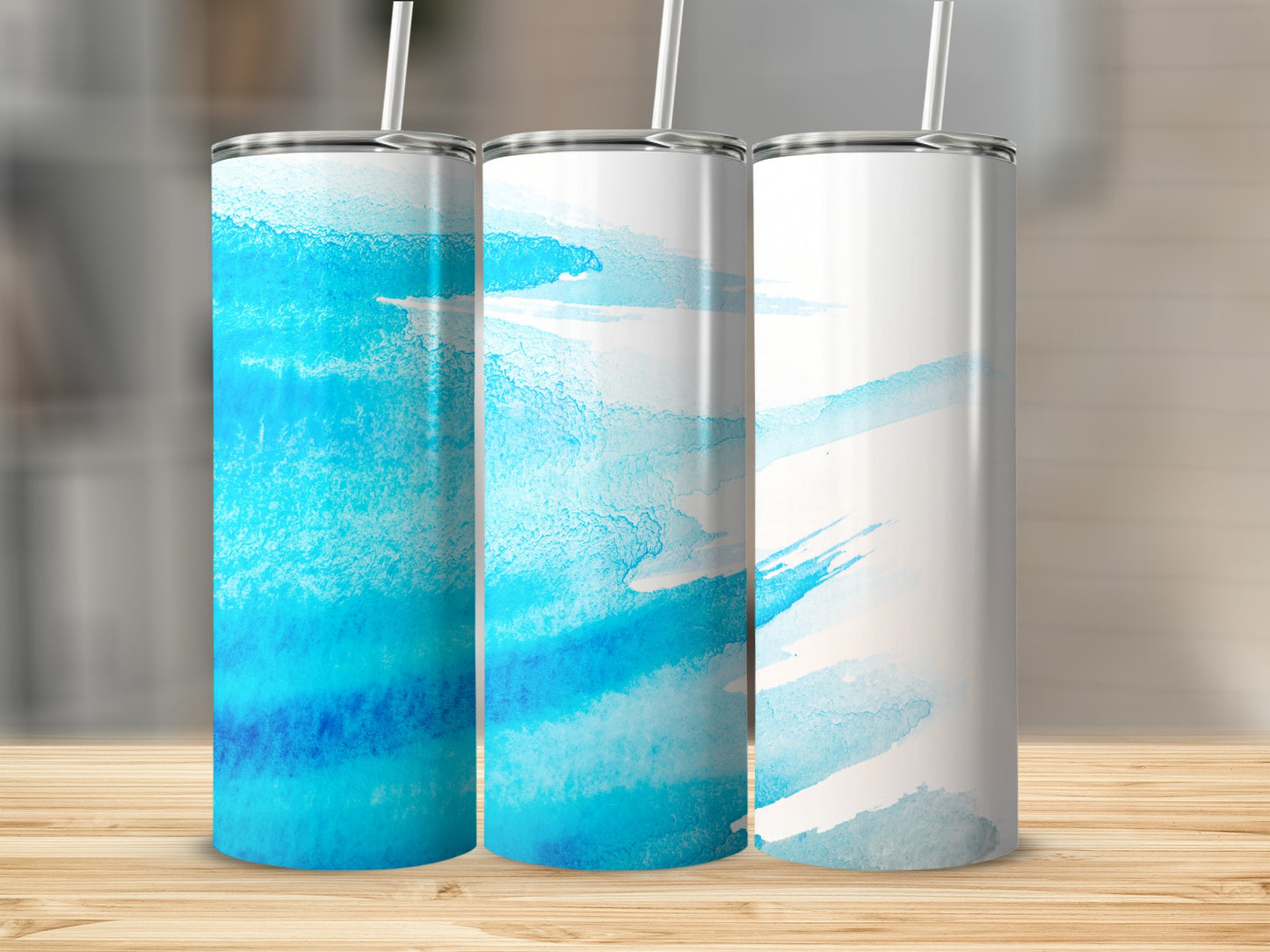 Three blue watercolor tumblers with white straws on a wooden surface.
